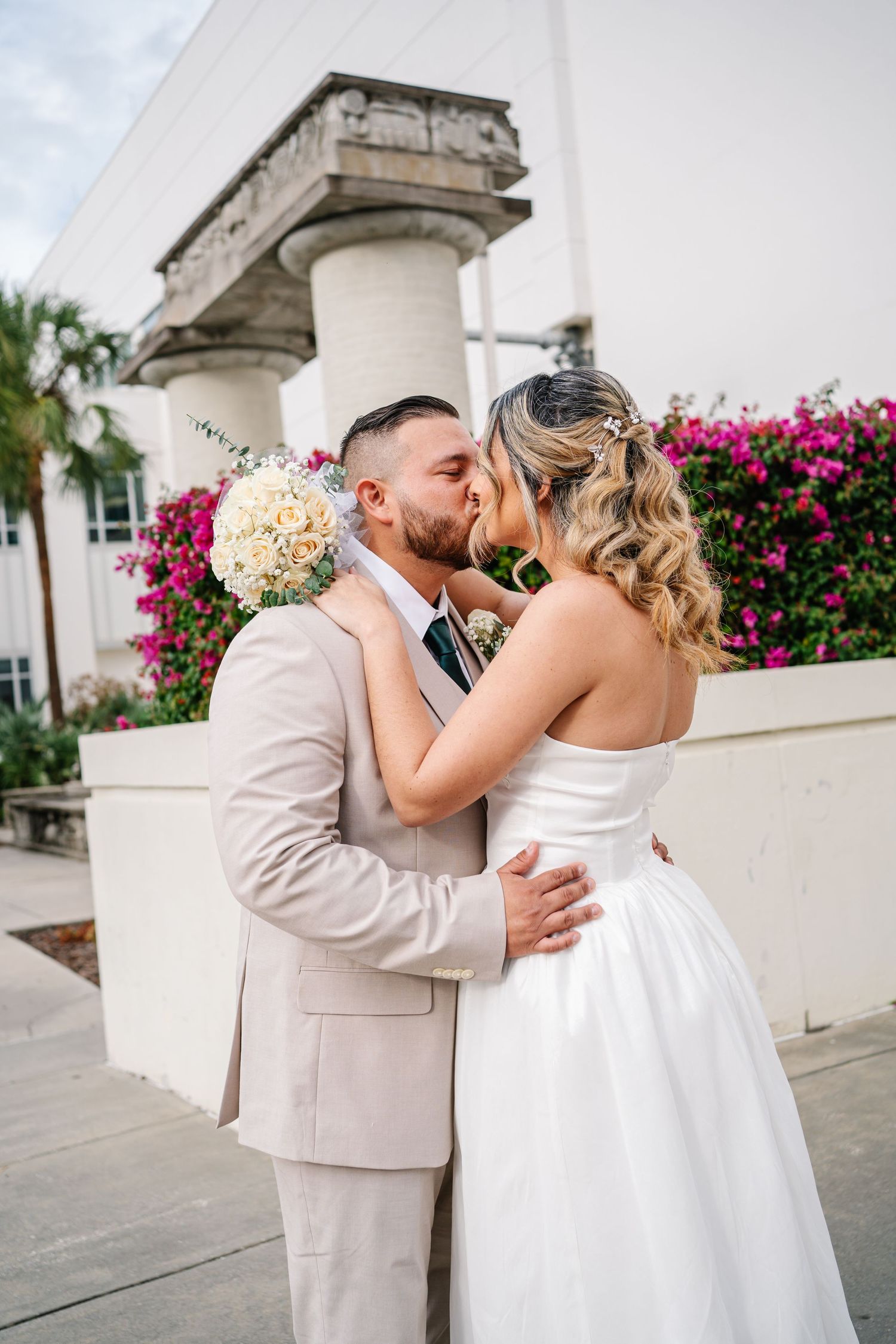 A couple shares a romantic moment outdoors with pink bougainvillea flowers in the background.