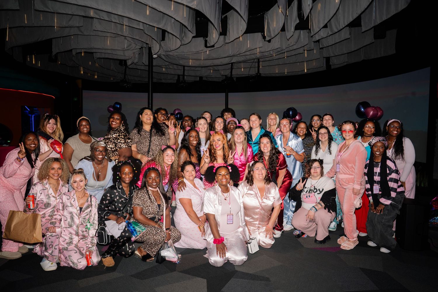 Large group of women in pajamas and sleepwear posing together at a pajama party event in a dark venue.