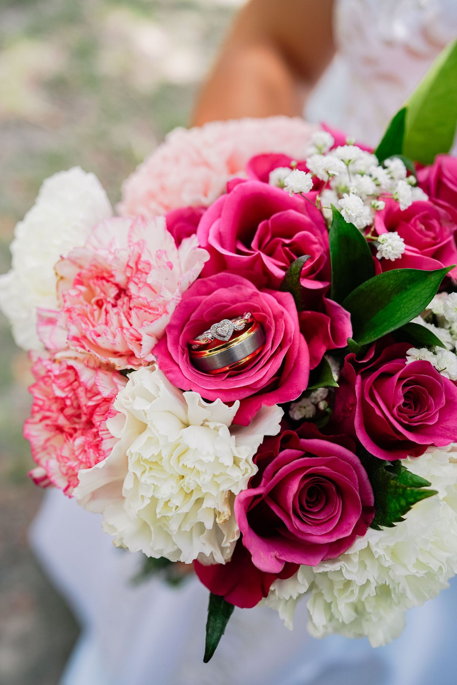 Bridal bouquet with pink roses, carnations, white hydrangeas, and wedding rings displayed elegantly.