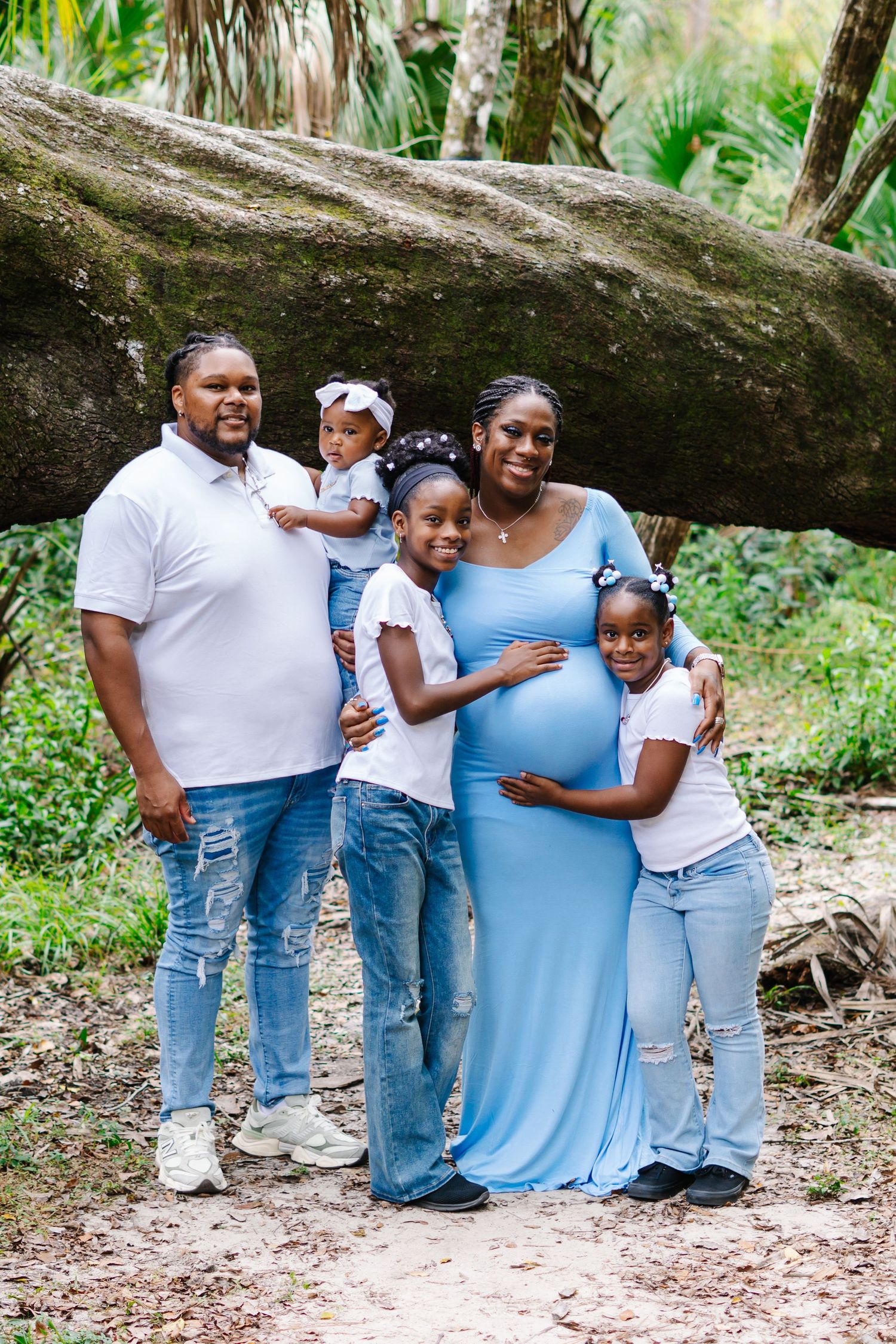 A family in coordinating blue and white outfits poses together in a natural outdoor setting.