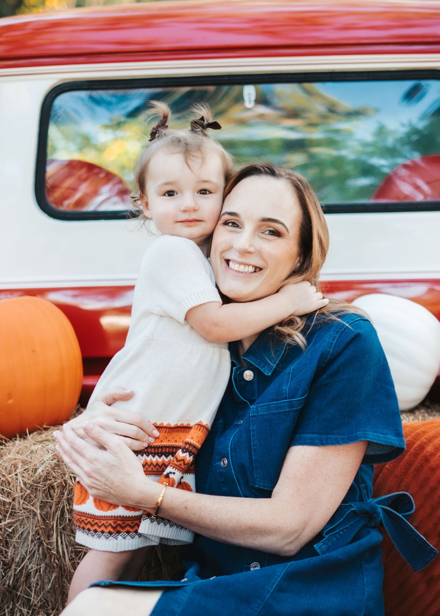 A fall themed photoshoot with pumpkins and hay bales around a vintage red truck.