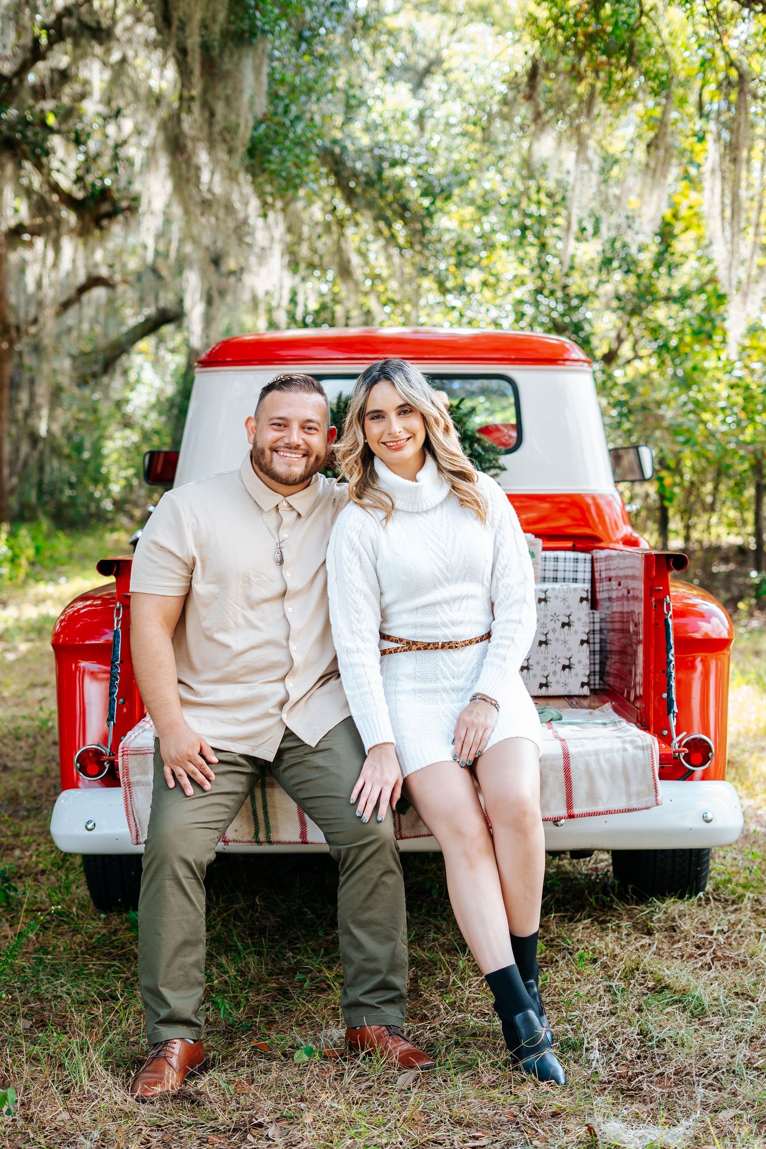 A couple sits together in the bed of a vintage red pickup truck.