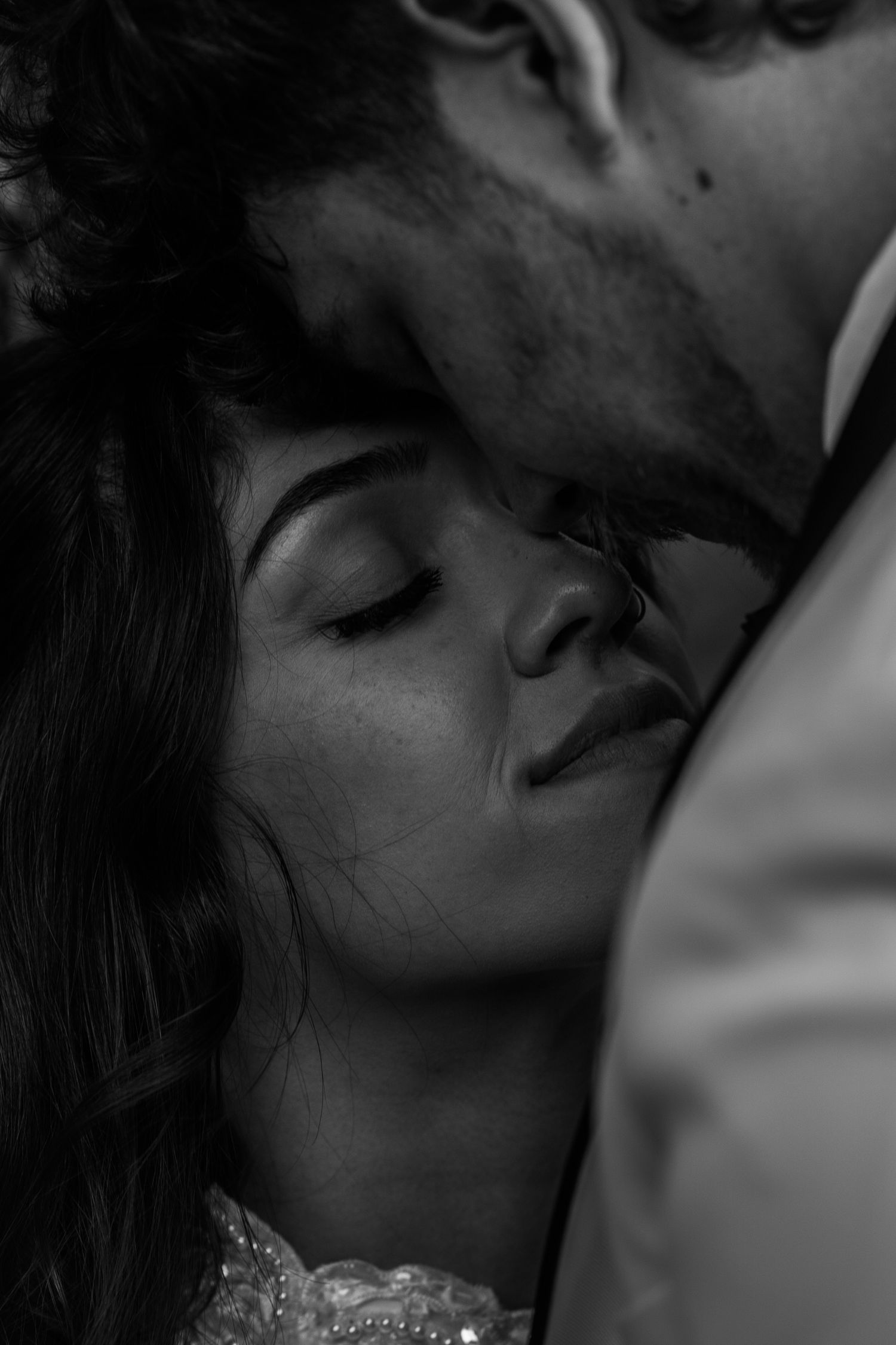 Black and white intimate couple portrait with woman closing eyes as man leans close, romantic fine art photography.