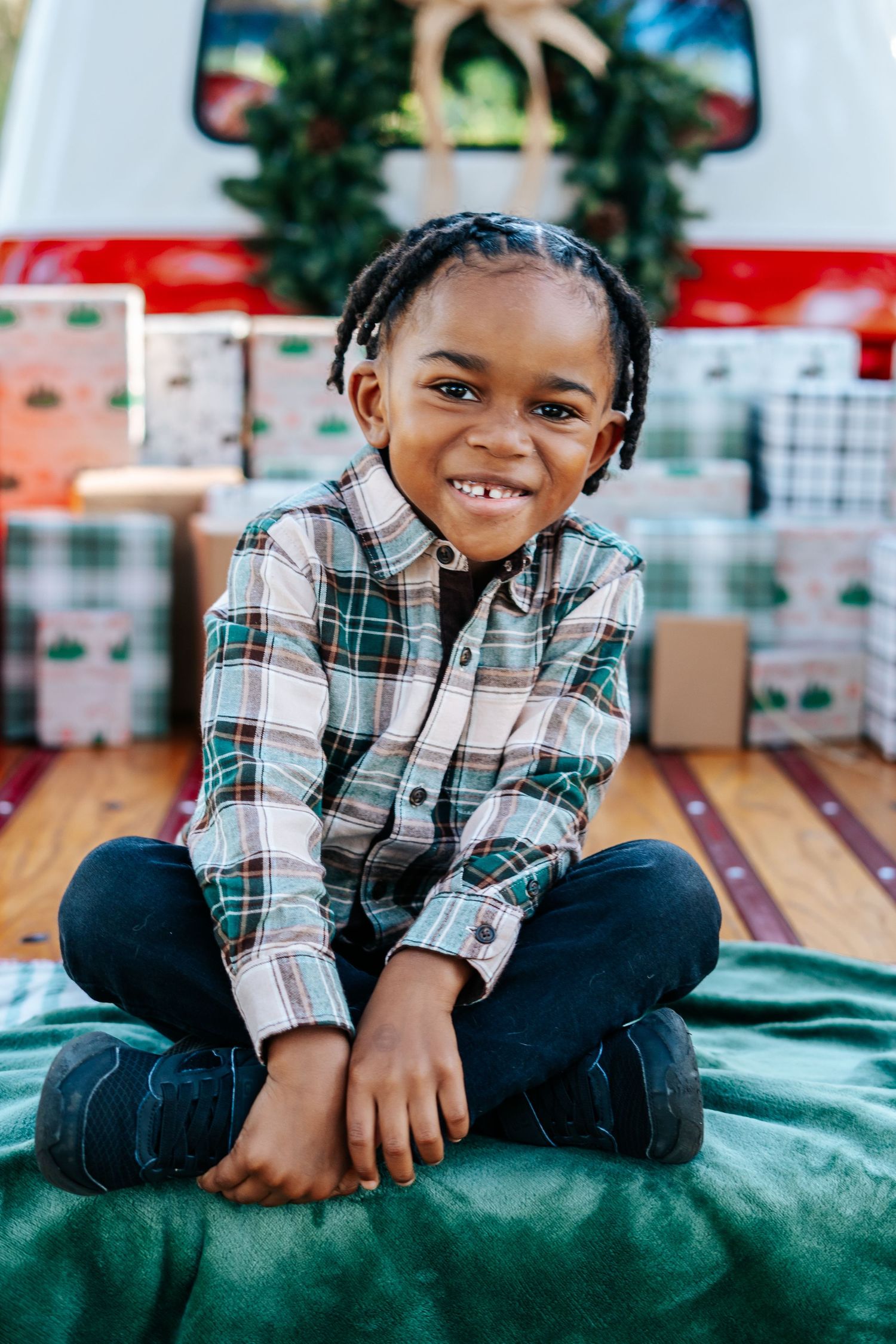 A young child in a plaid shirt and jeans lies on a green cushioned surface in a playful pose.