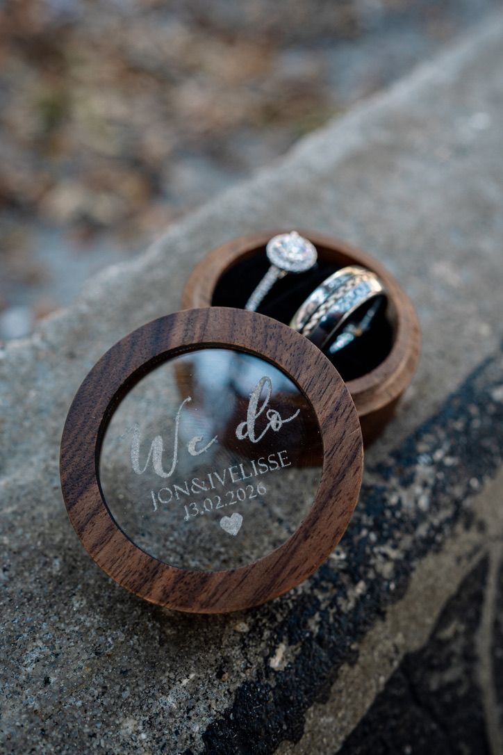 Wedding rings displayed in a custom wooden ring box with 'We do' text engraved on glass lid.