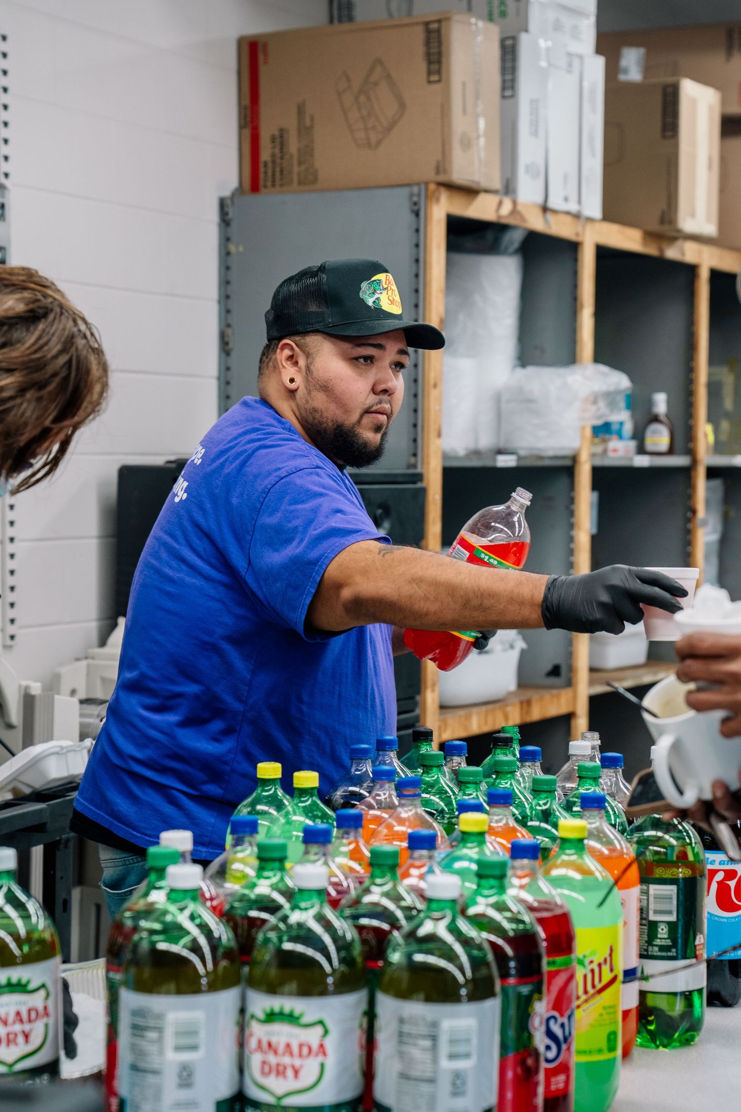 Man in blue shirt and cap serving drinks at a table lined with Canada Dry and Squirt soda bottles.