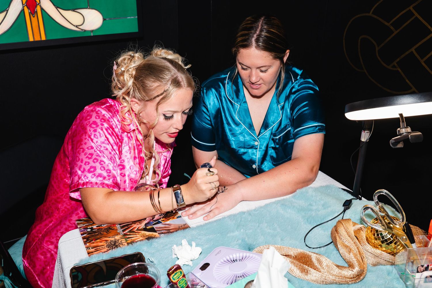 Two women in colorful satin pajamas signing autographs at a table with a snake nearby.