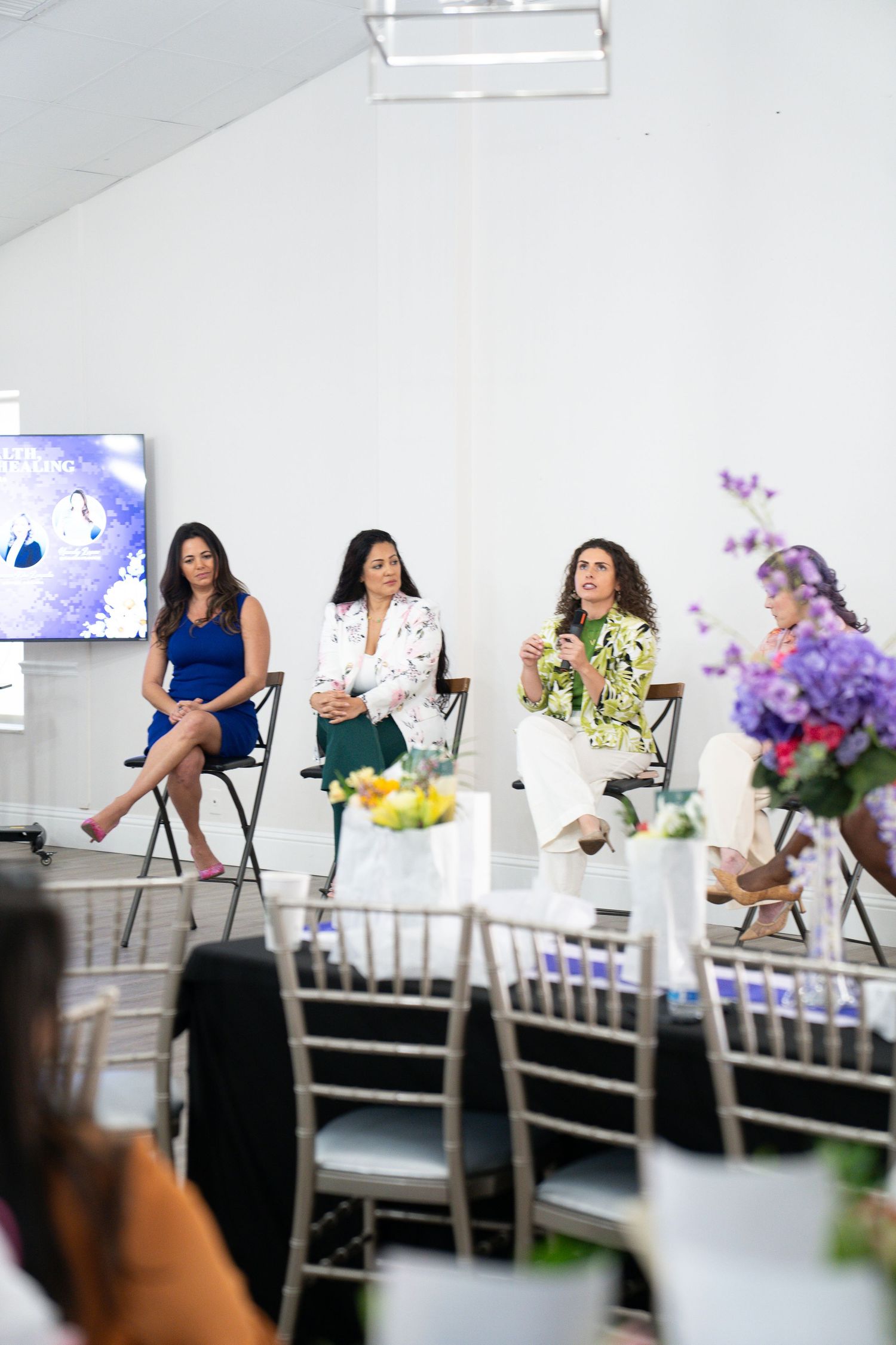 Three women seated on stage during panel discussion at bright white indoor event venue.
