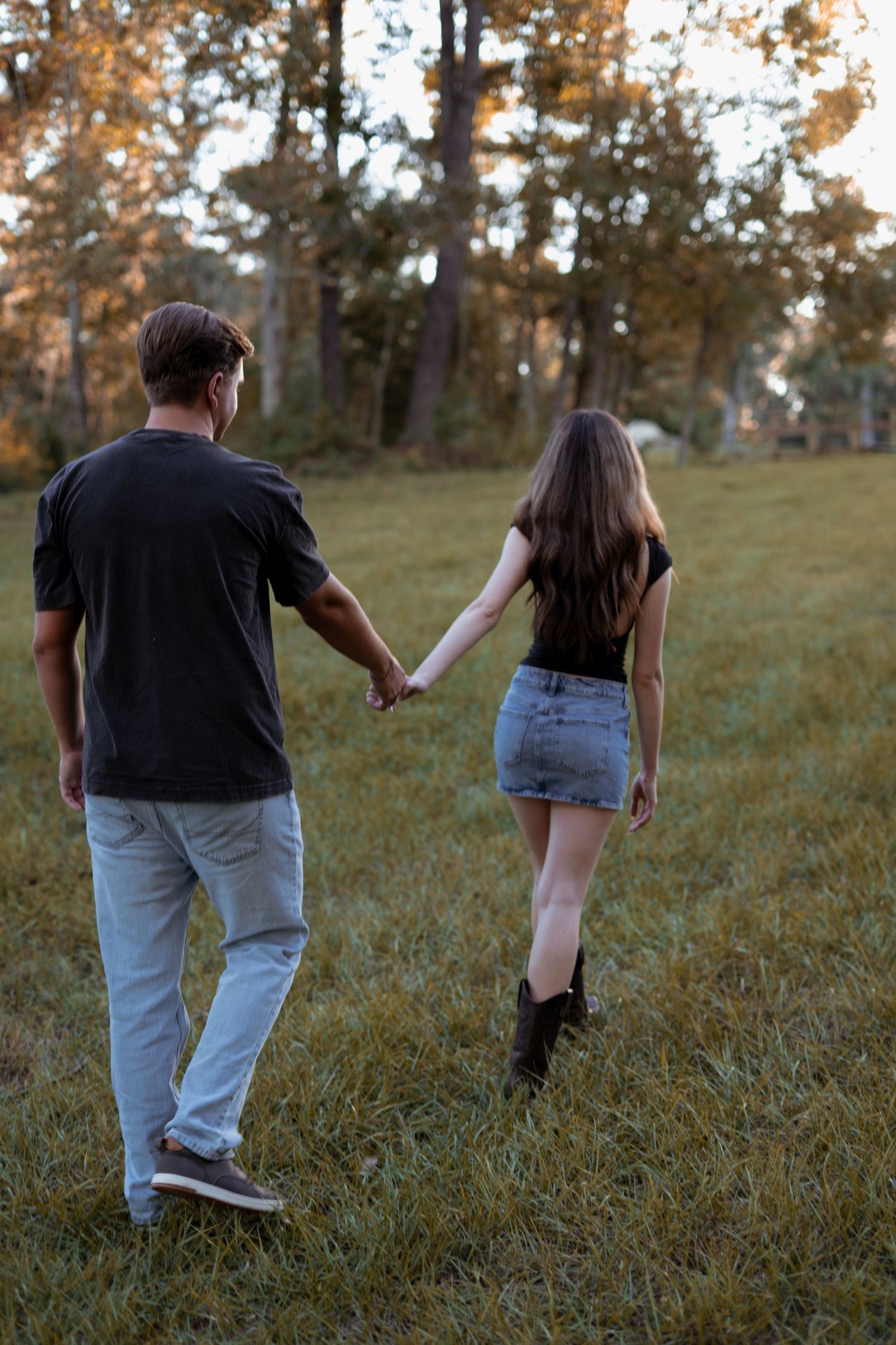 A couple walks together through a grassy field during golden hour.