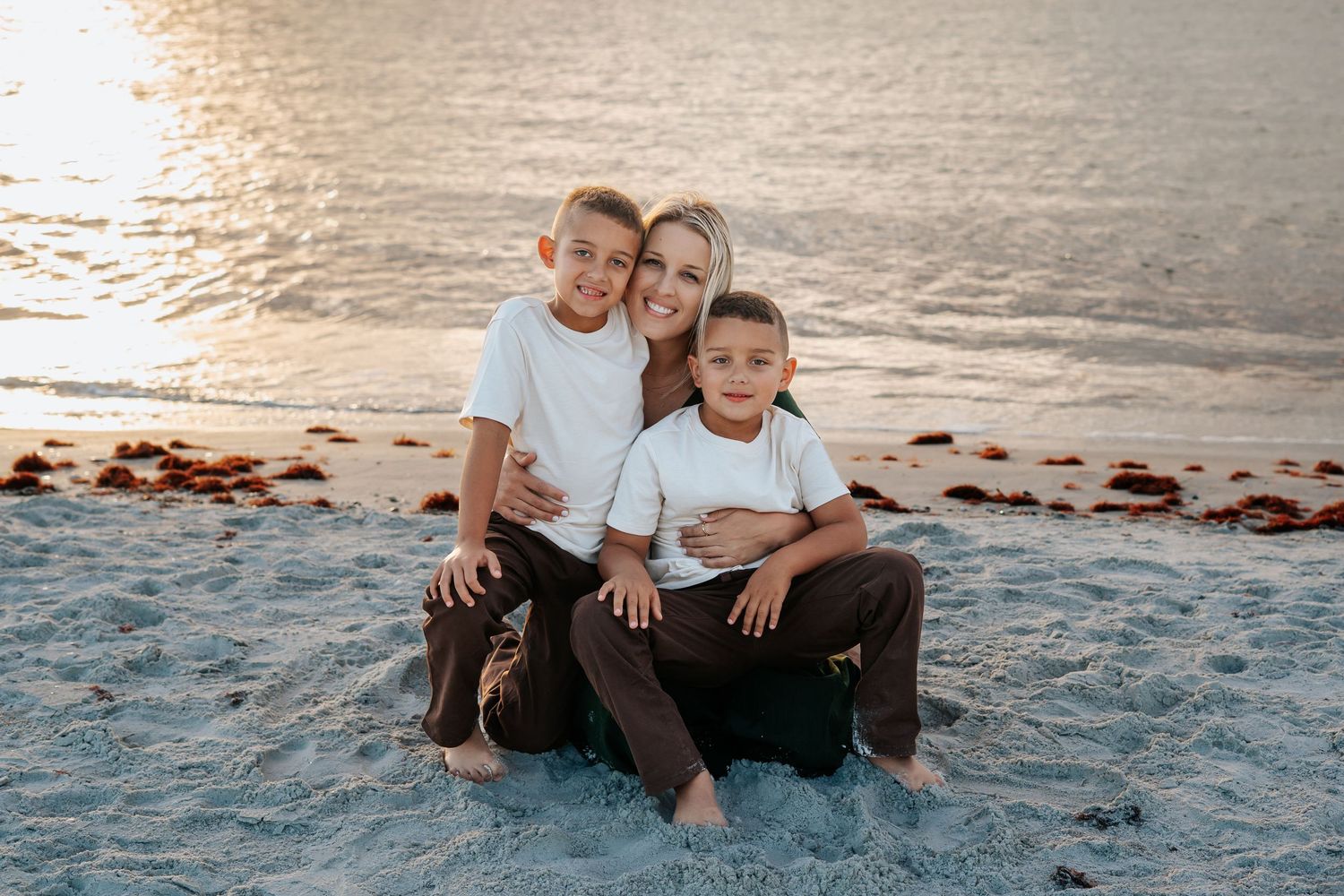 A family sits together on a sandy beach at sunset, enjoying a peaceful moment.