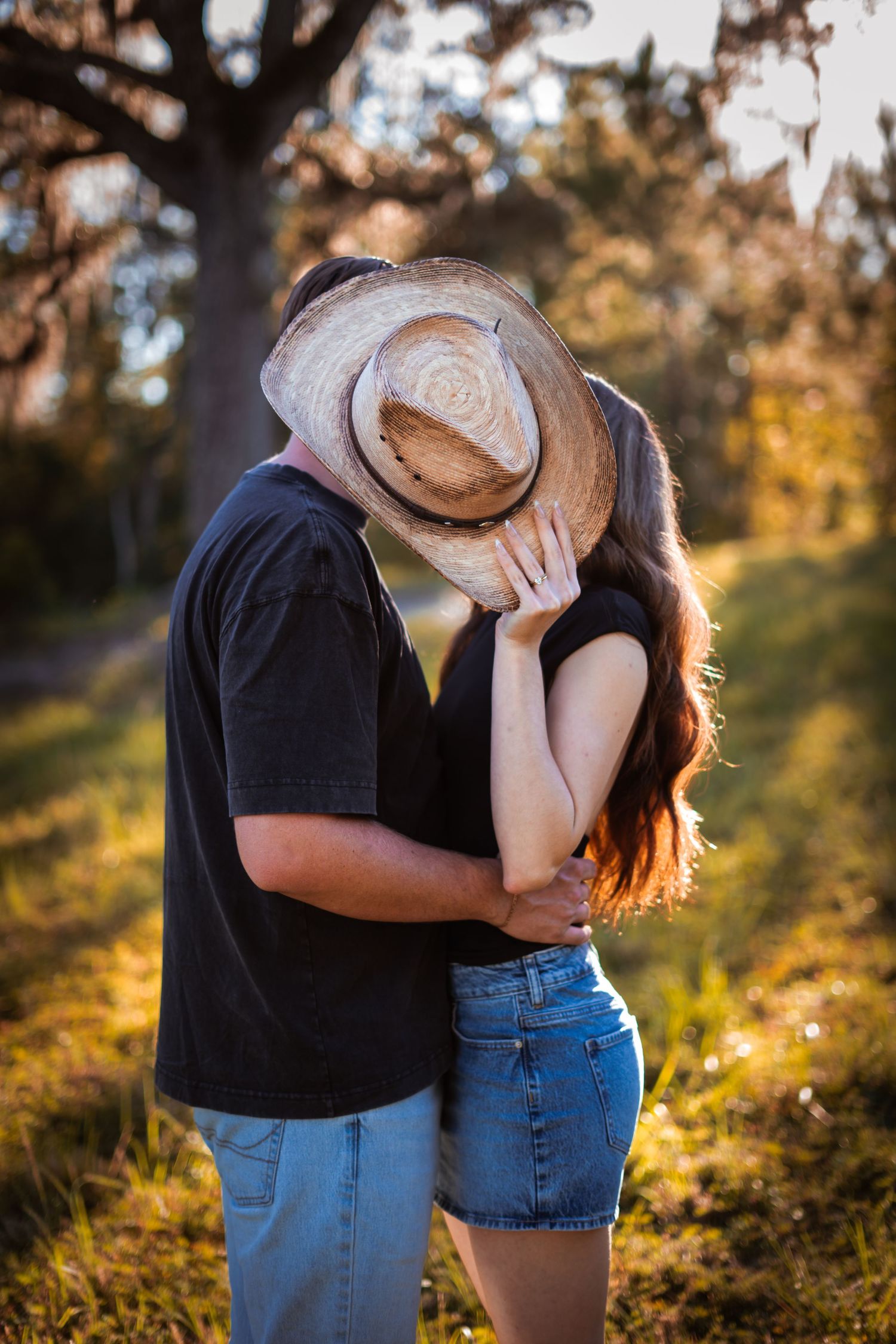 A couple embracing in warm sunset light with one wearing a cowboy hat.