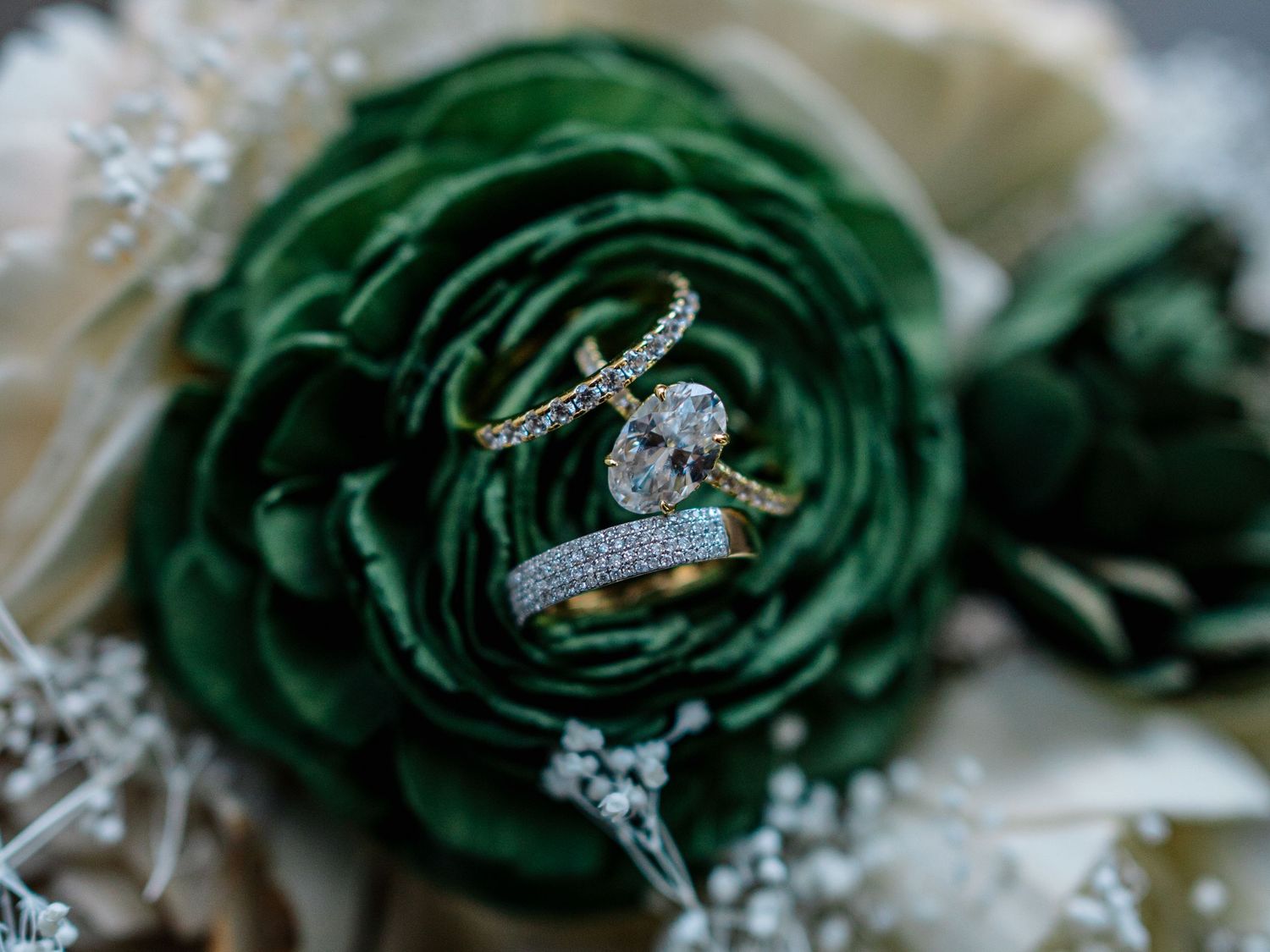 Diamond engagement ring and wedding bands resting elegantly on a lush green ranunculus flower in a bridal bouquet.