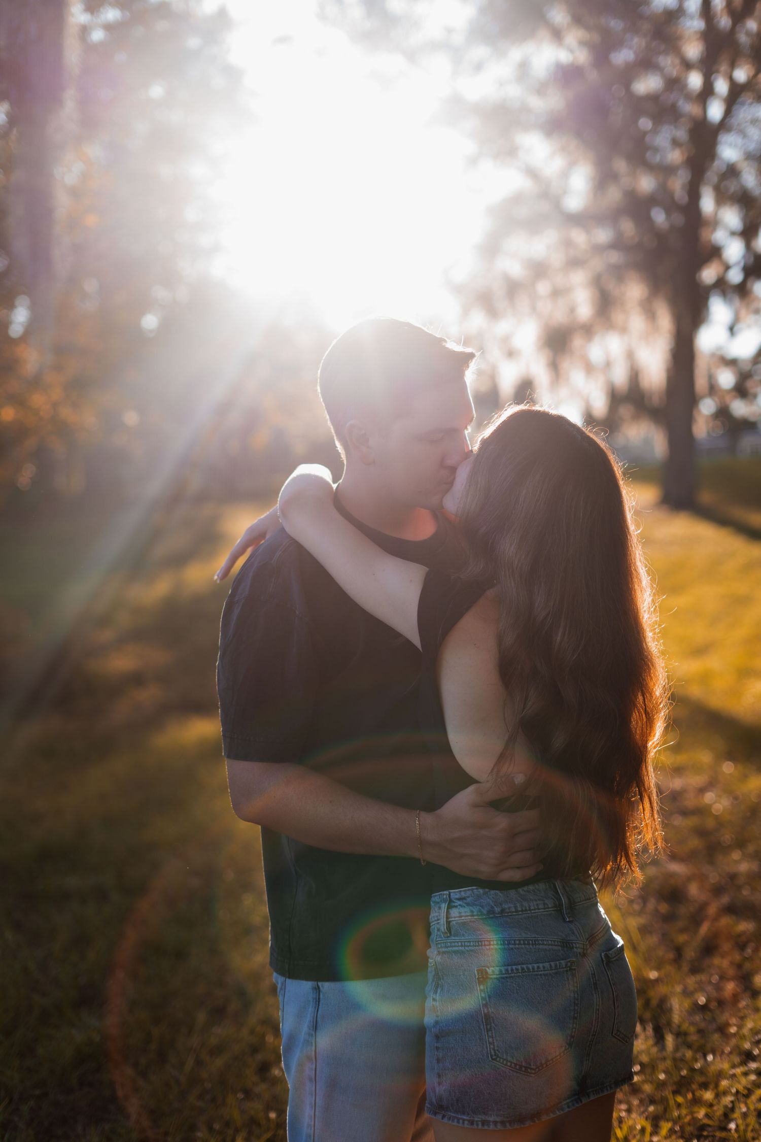 A couple sharing an intimate moment in golden sunlight on a grassy hillside.