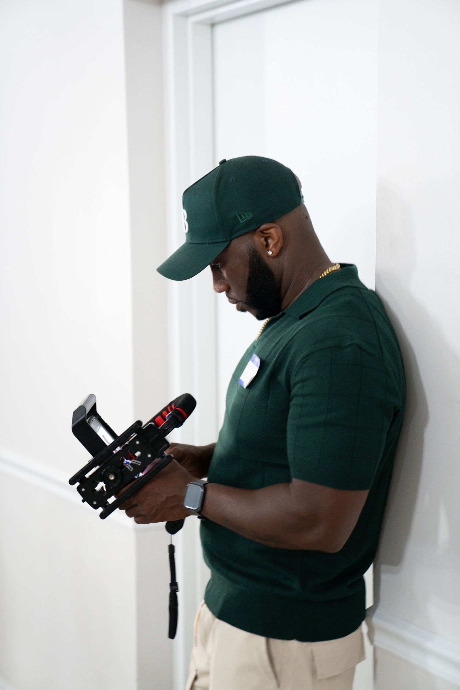 Man in green polo and cap adjusting professional camera gimbal stabilizer indoors.