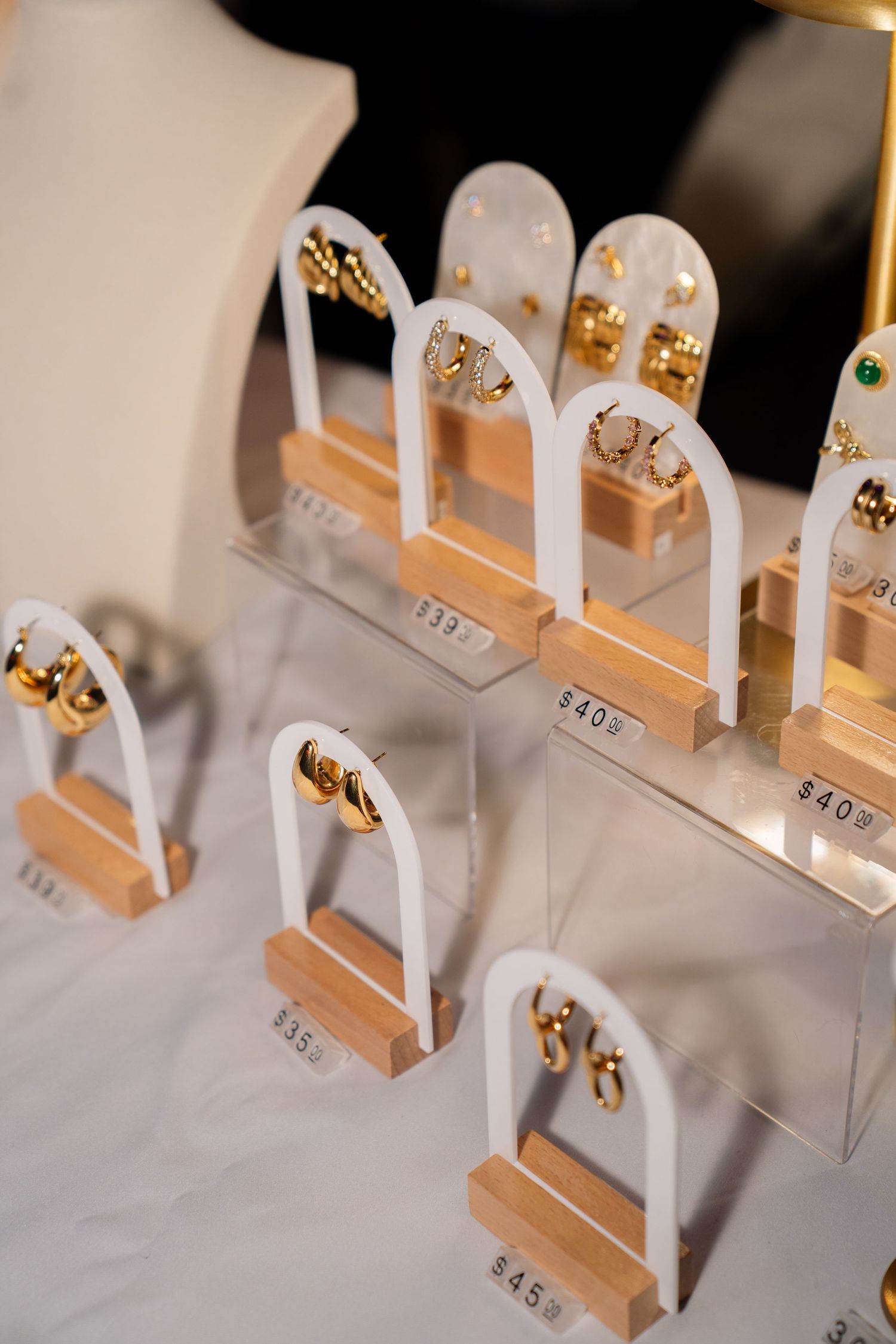 Gold earrings displayed on white arch stands with price tags at a jewelry market booth.