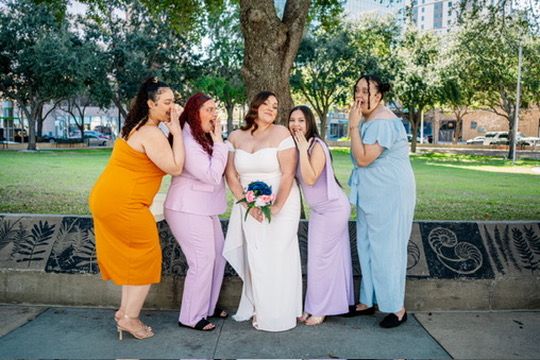 A group in coordinating pink and blue outfits poses together outdoors for casual photos in a park setting.