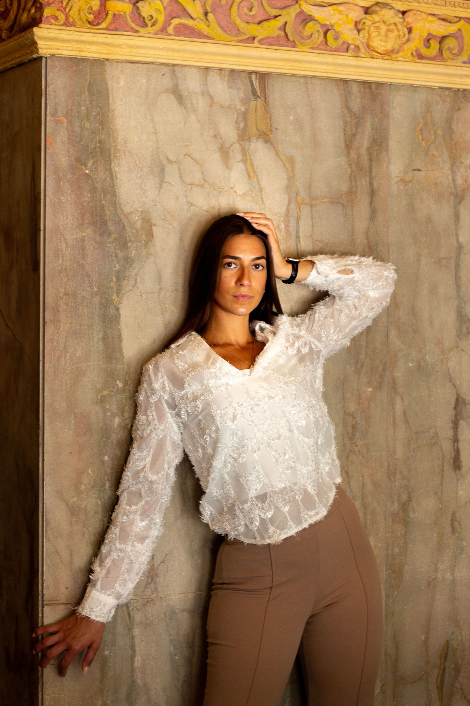 A fashion portrait series showing a model in a white ruffled blouse and brown pants posing against a textured wall.