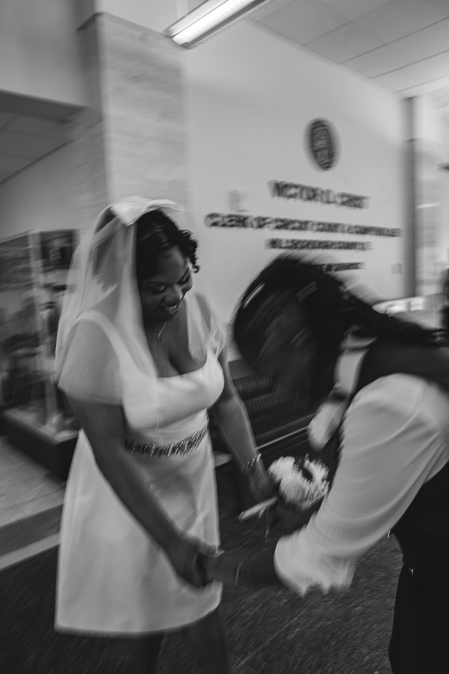 Black and white photo of bride in veil dancing joyfully at courthouse wedding ceremony.
