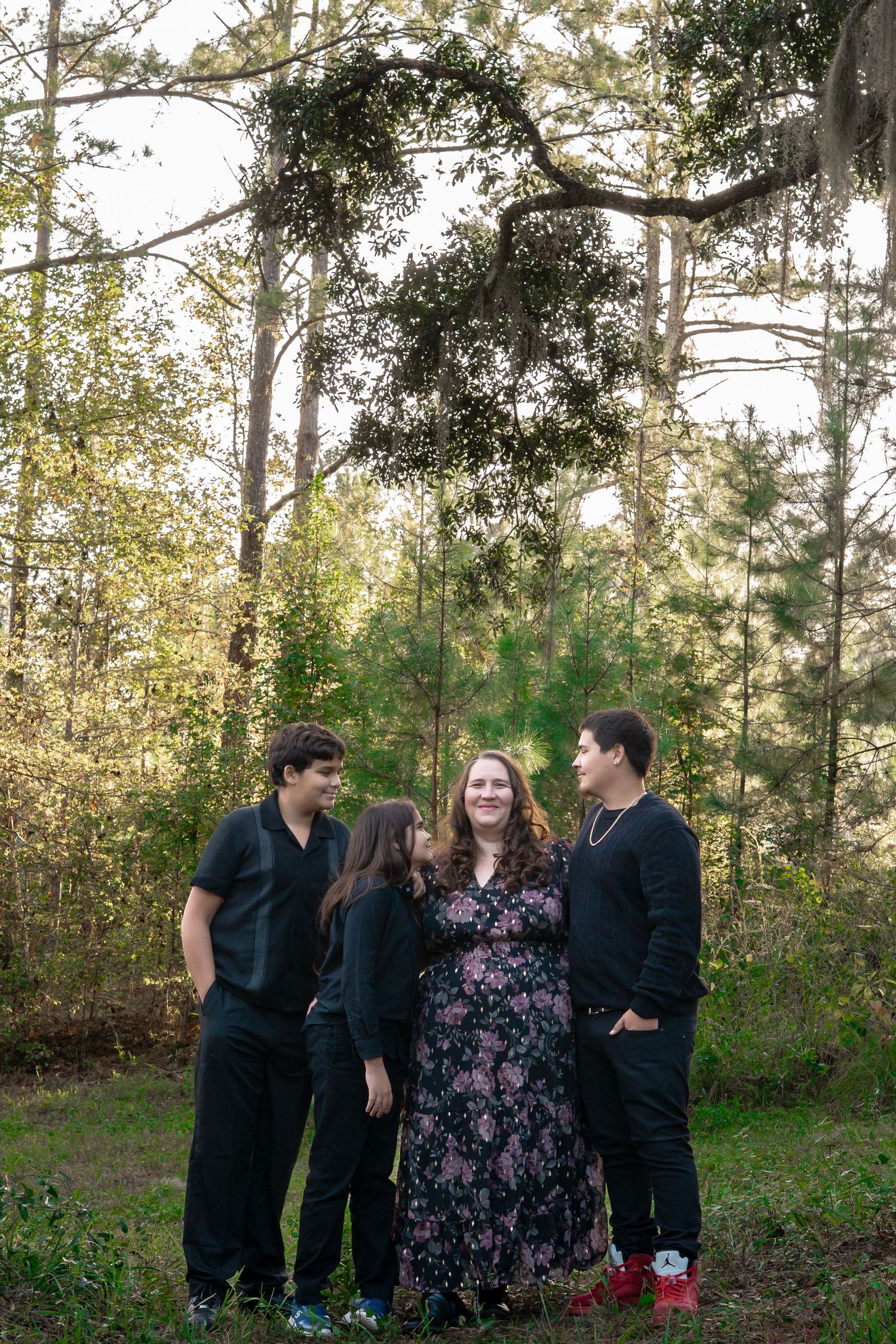 Three people in dark clothing having a conversation under tall trees.