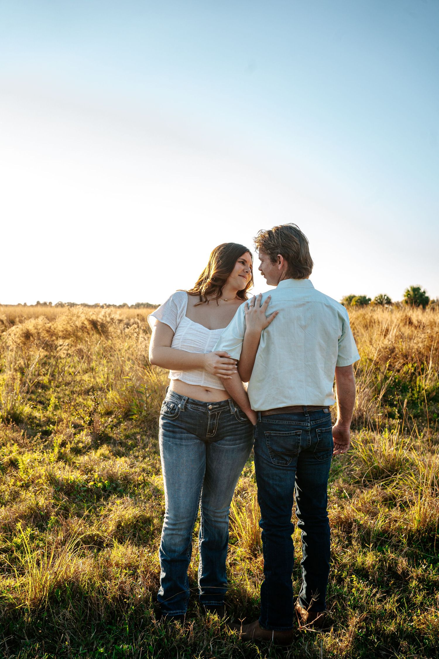 Couple sharing a romantic moment in a sunlit golden field, wearing jeans and casual tops during golden hour.