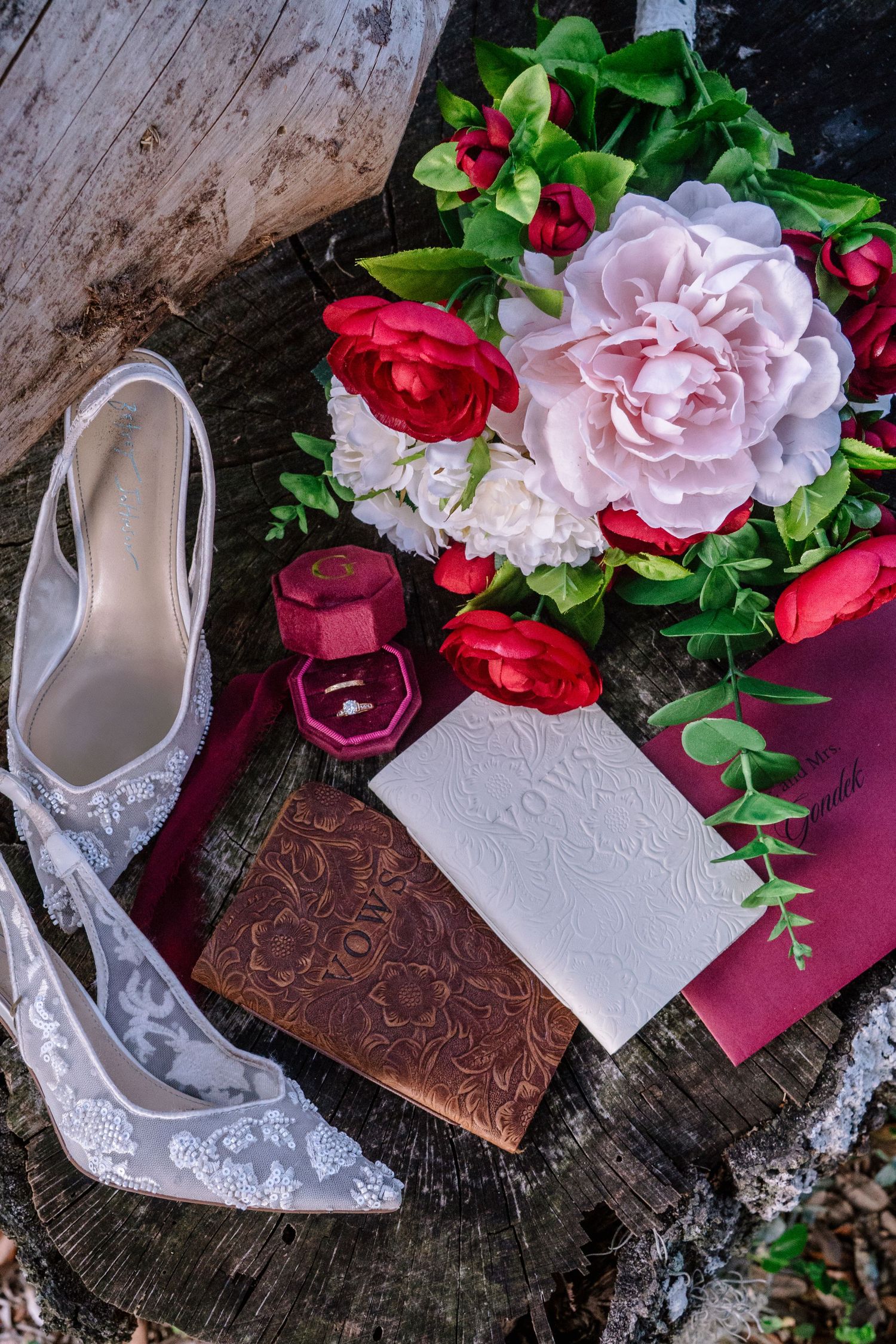 Elegant wedding flat lay with lace heels, floral bouquet, ring box, and invitation on rustic wood.