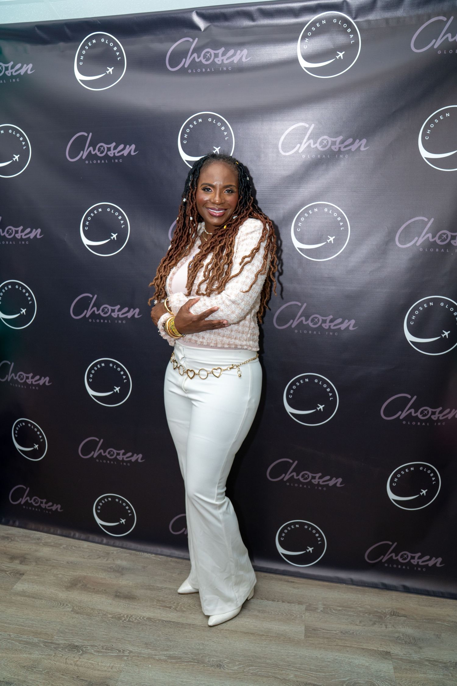 Woman in white flared pants and pink top posing at Chosen Directors event backdrop.