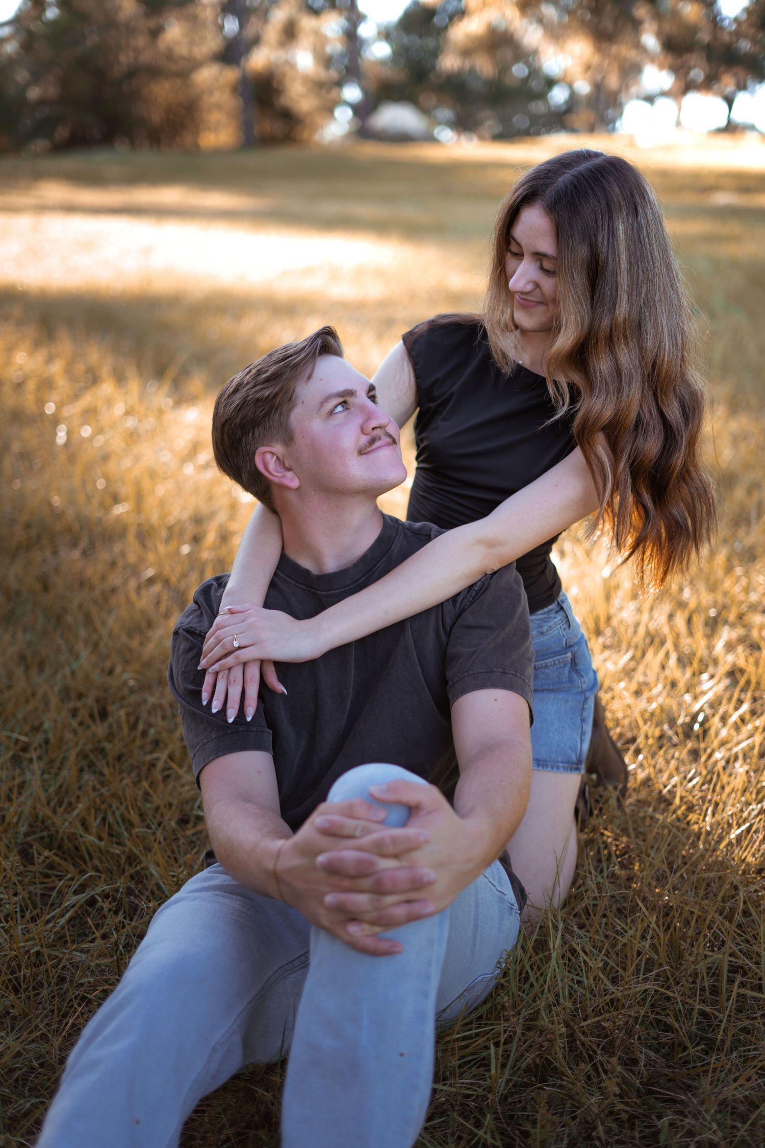 A playful couple embraces in a golden field during sunset, sharing laughter and joy.