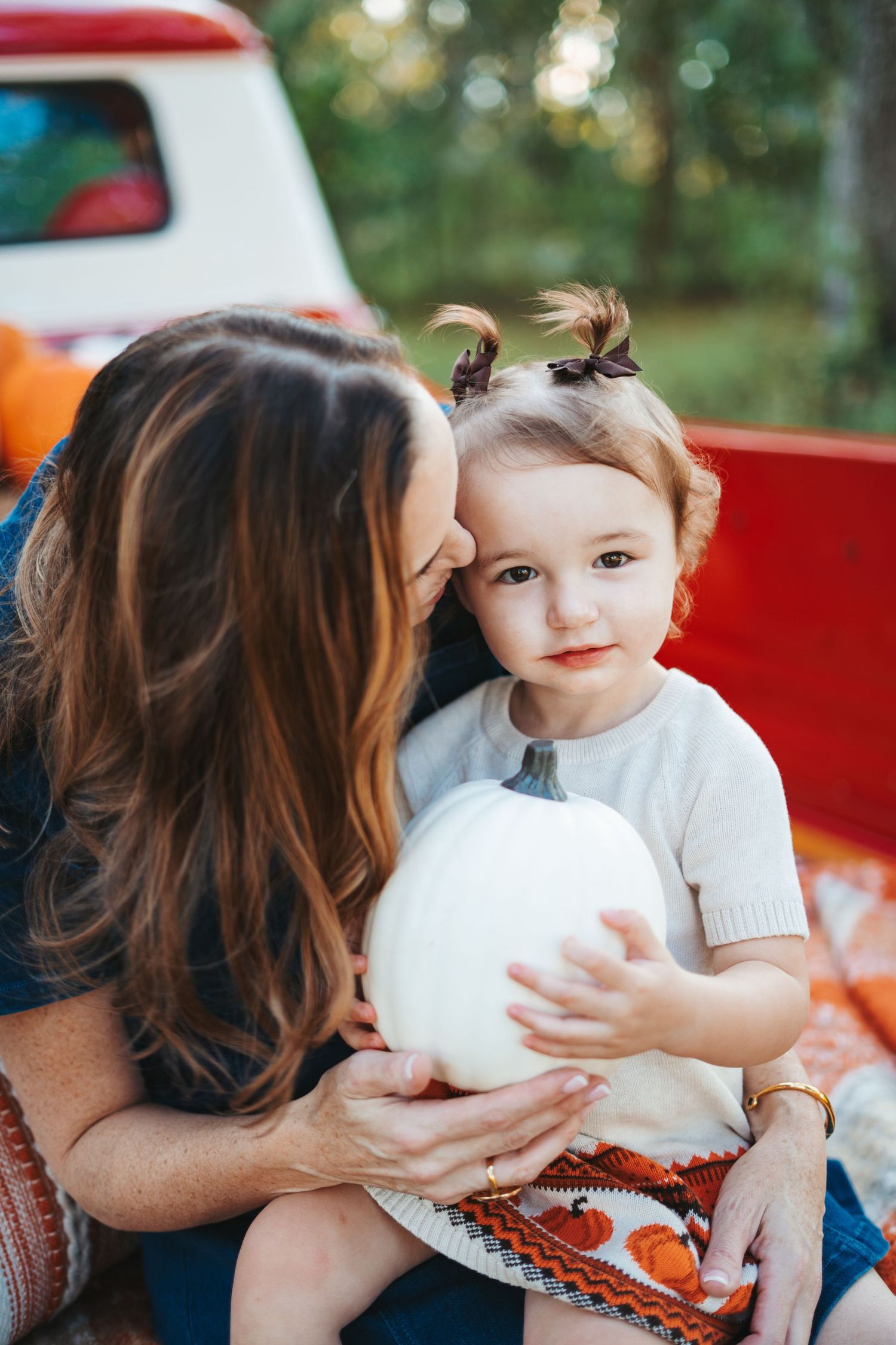 Tender moment captured with white pumpkin and fall-themed clothing near a red vintage truck.