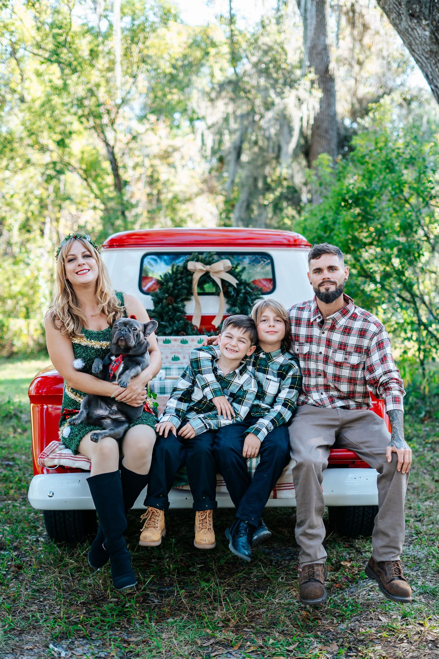 Family in coordinated outfits poses on vintage red pickup truck tailgate for holiday photos.