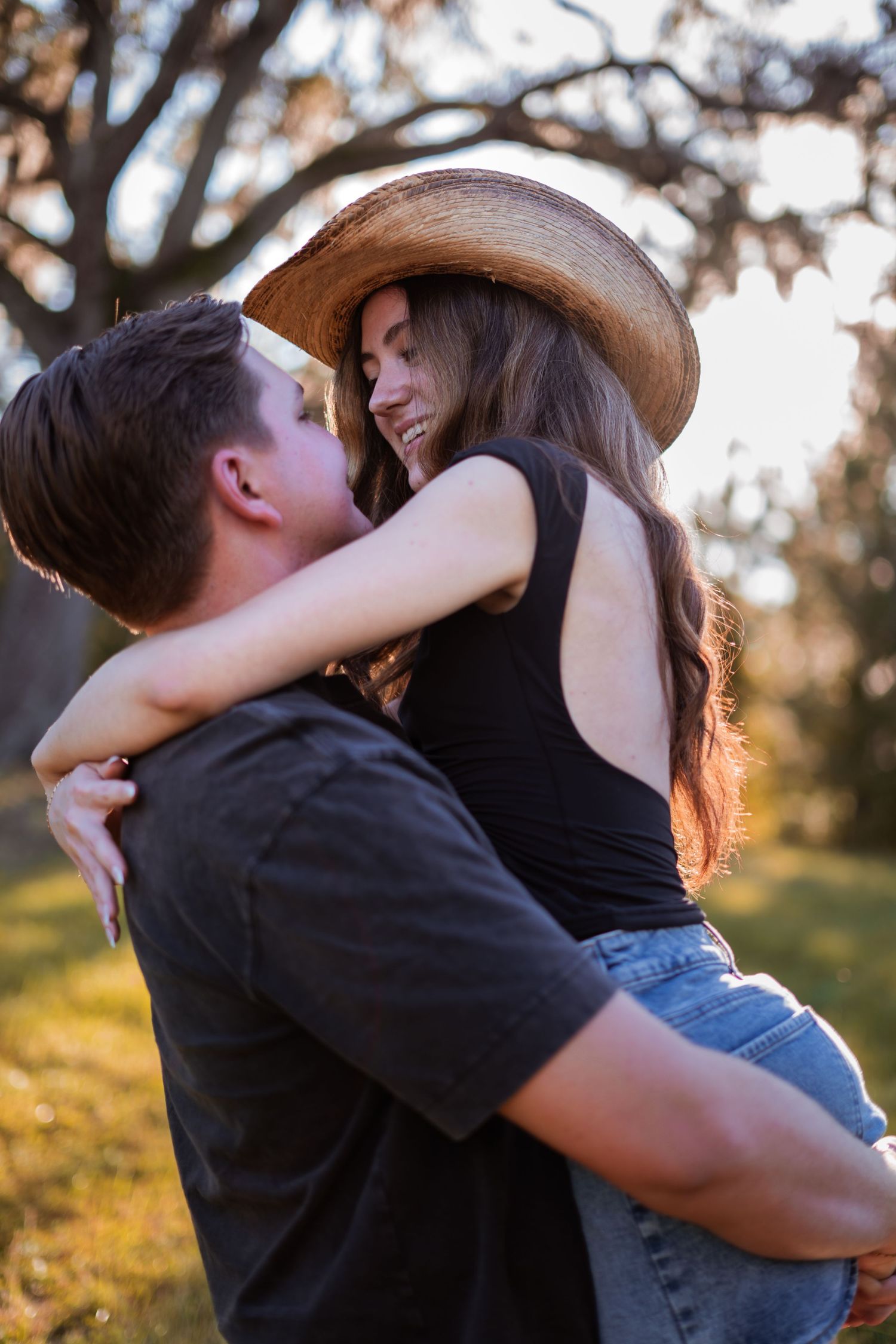 A romantic couple embraces in a sun-dappled outdoor setting.