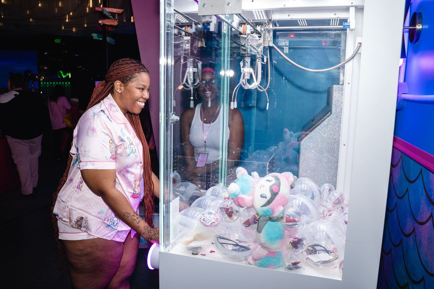Woman in pink outfit playing a claw machine filled with stuffed animals at an arcade.