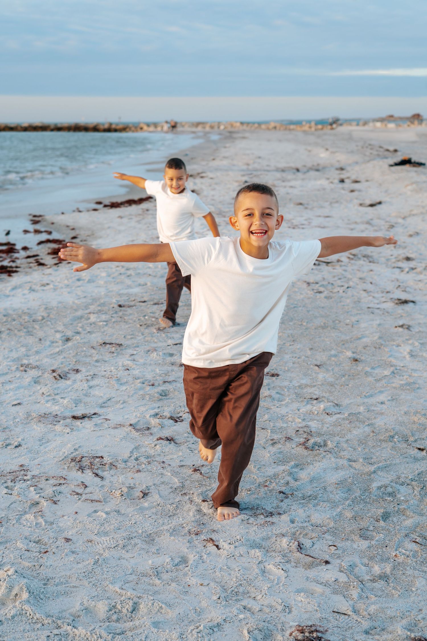 A child plays joyfully on the beach with arms spread wide like wings.