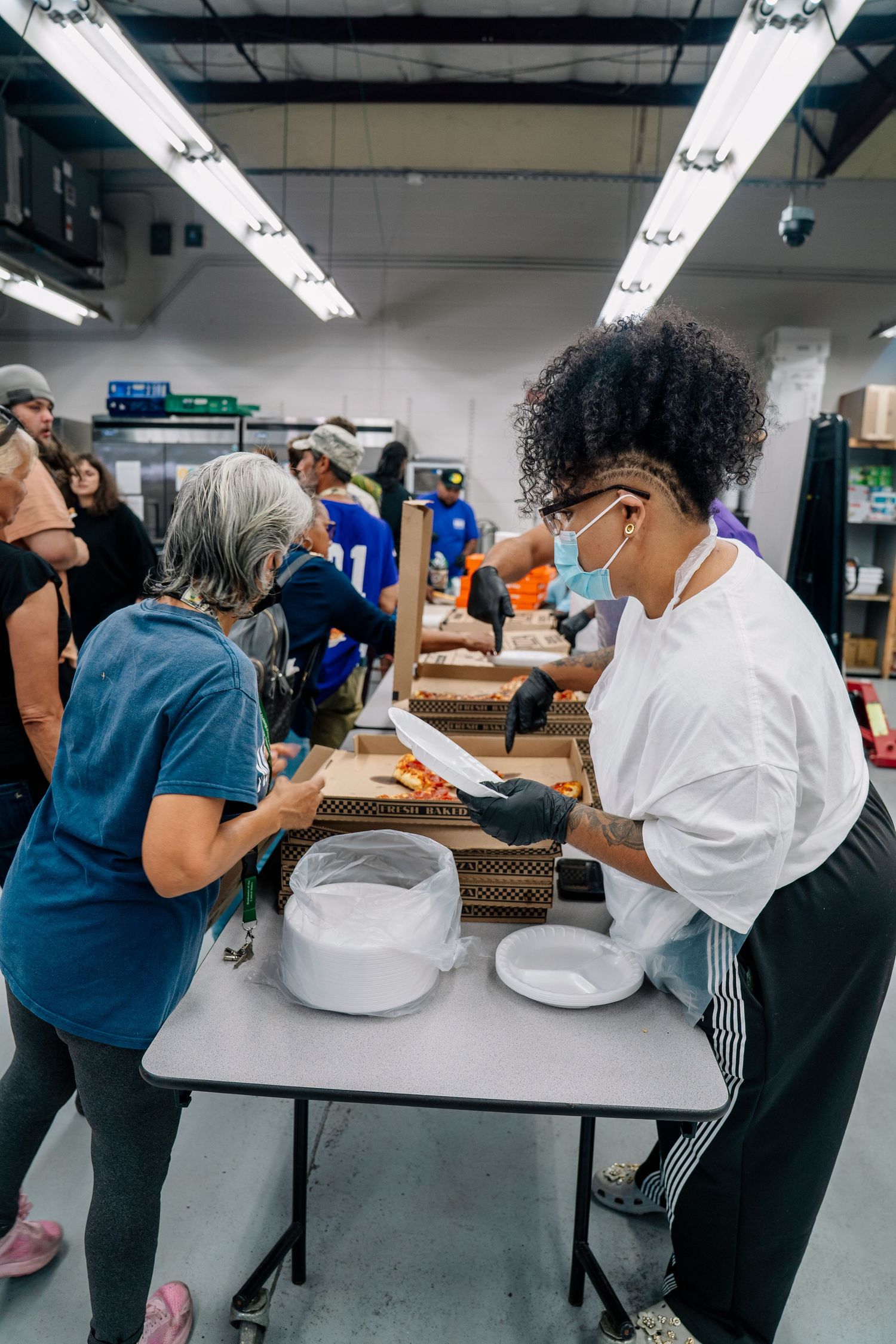 Volunteers wearing masks pack food boxes at an indoor community food distribution center.