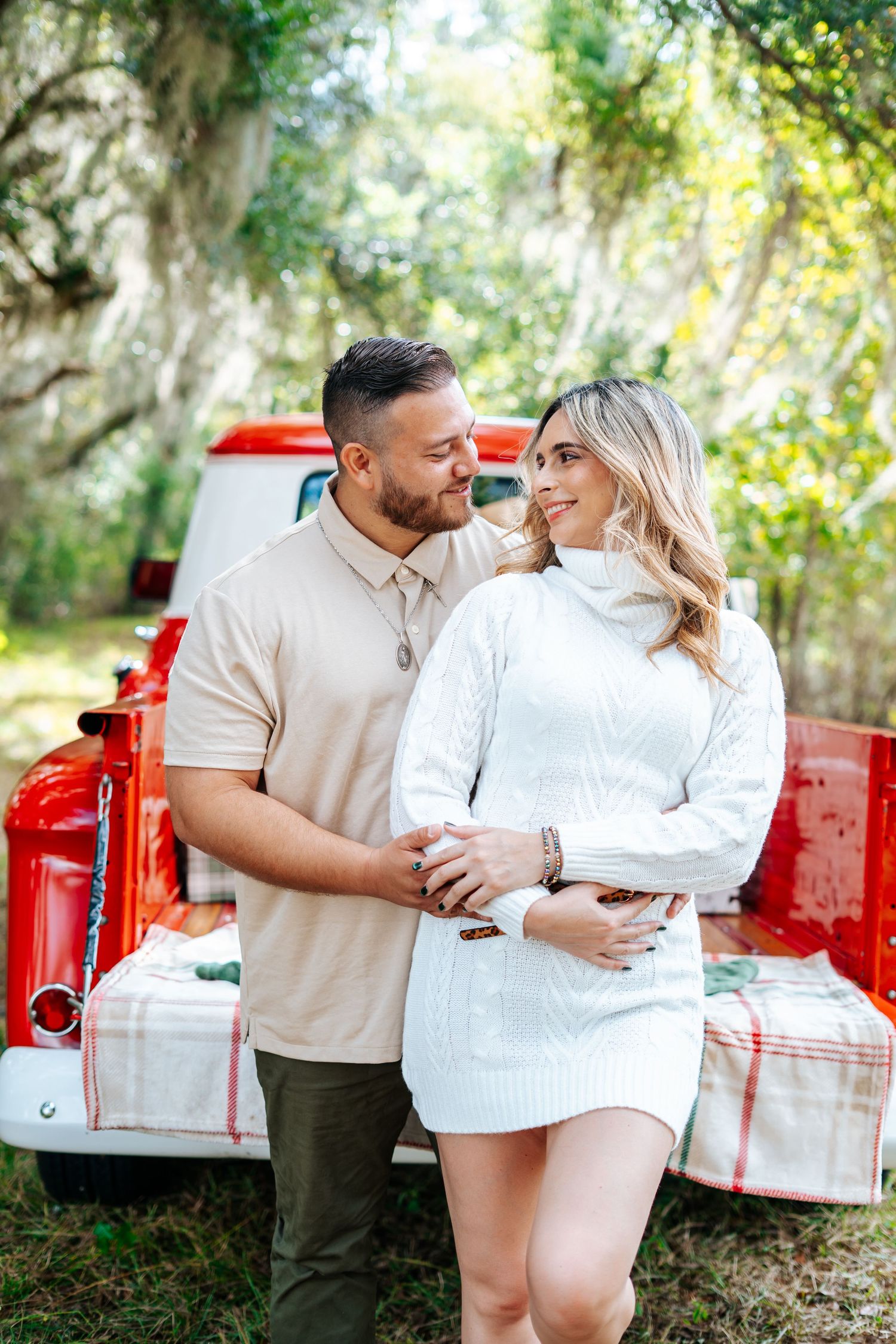 A couple shares an intimate moment by a red vintage truck.