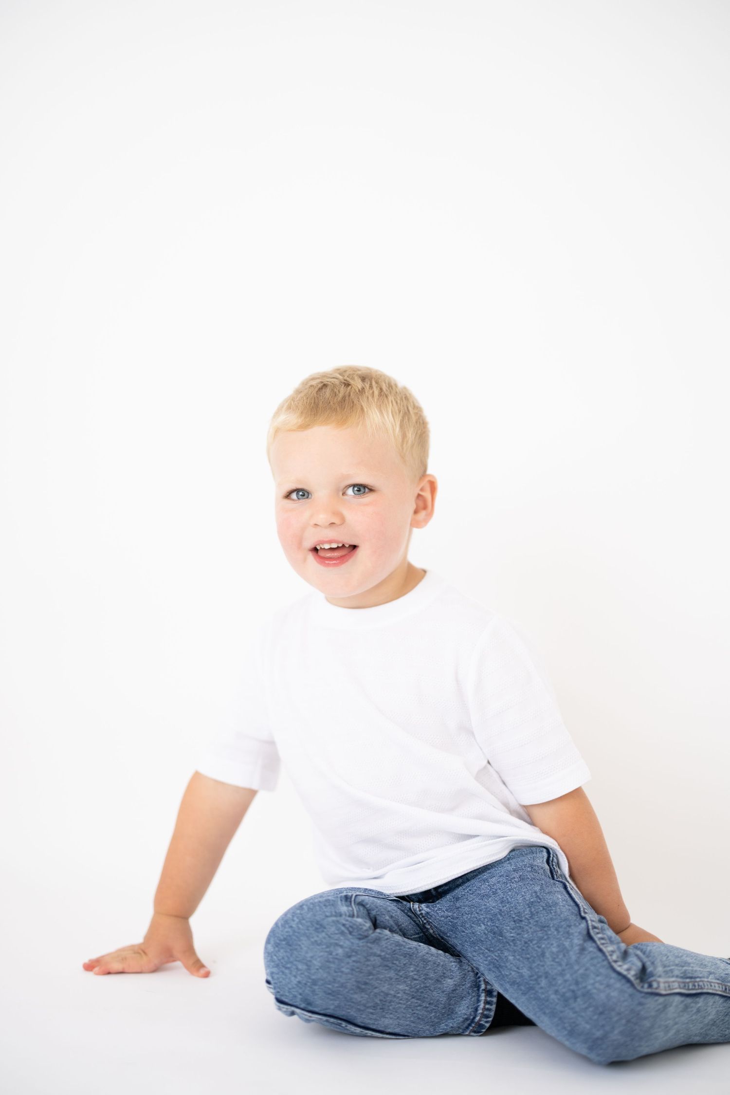 Young child in casual white t-shirt and jeans poses on white studio background.