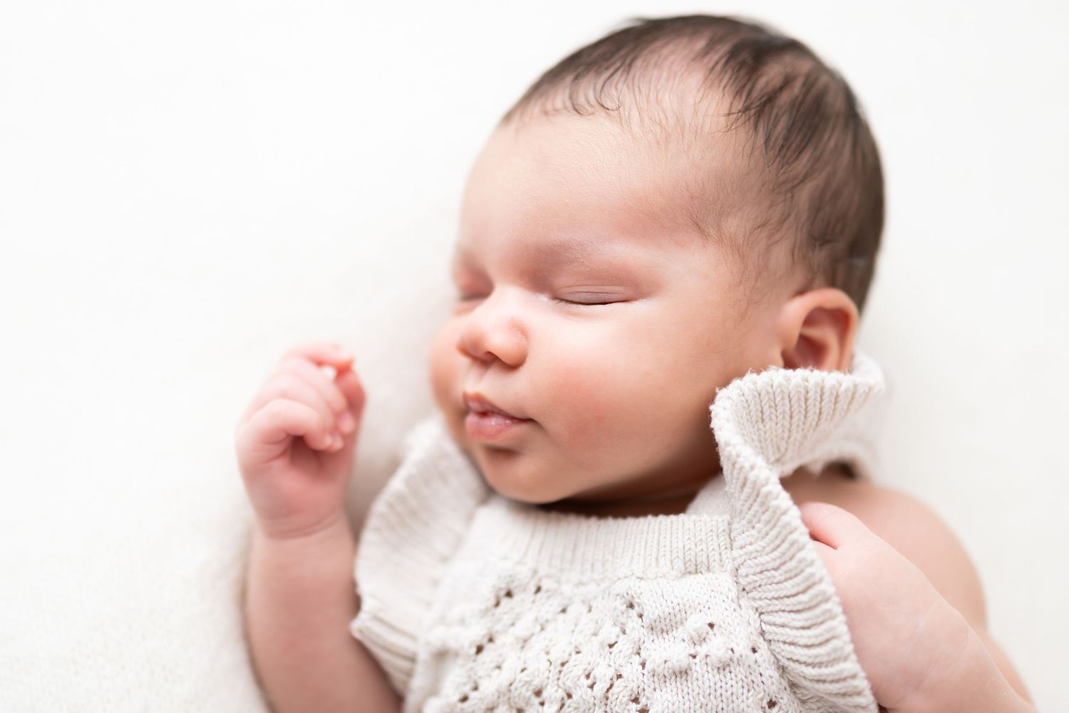 Close-up portrait of sleeping infant in white knit clothing on light background.