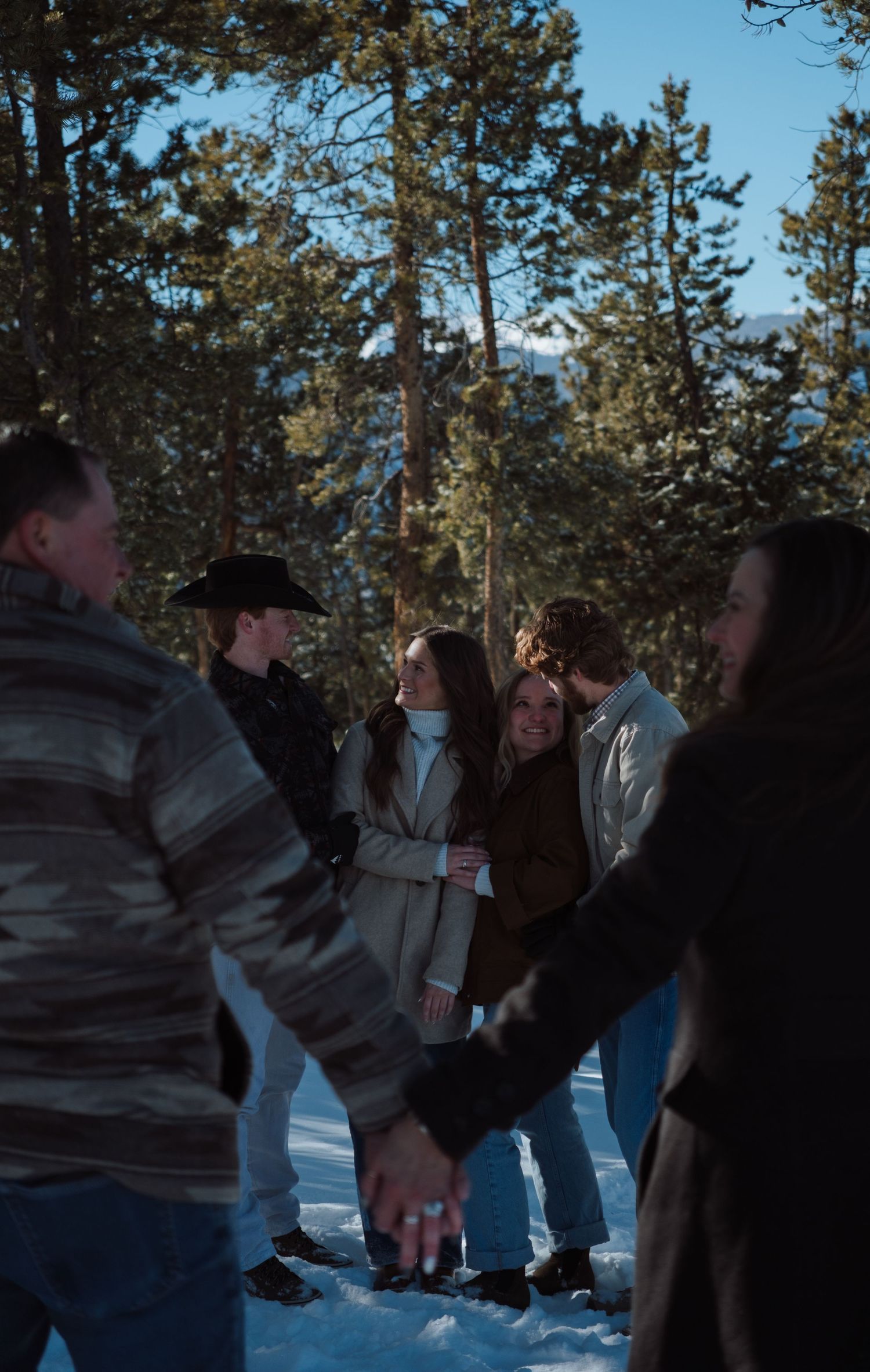 Group of friends holding hands in a snowy forest clearing on a sunny winter day.