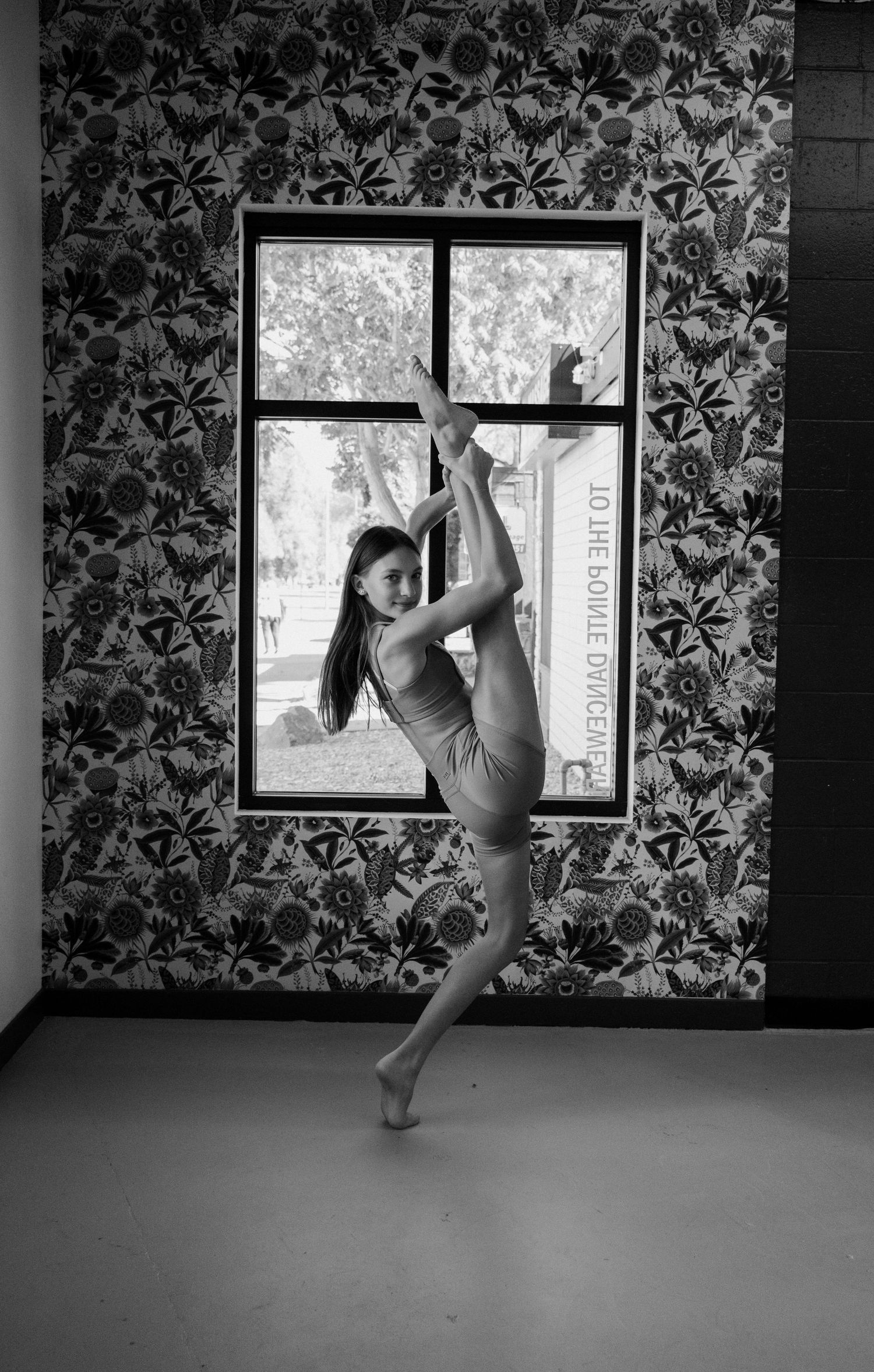 A dancer performs a dynamic sequence of high kicks against a floral wallpapered background in black and white photos.