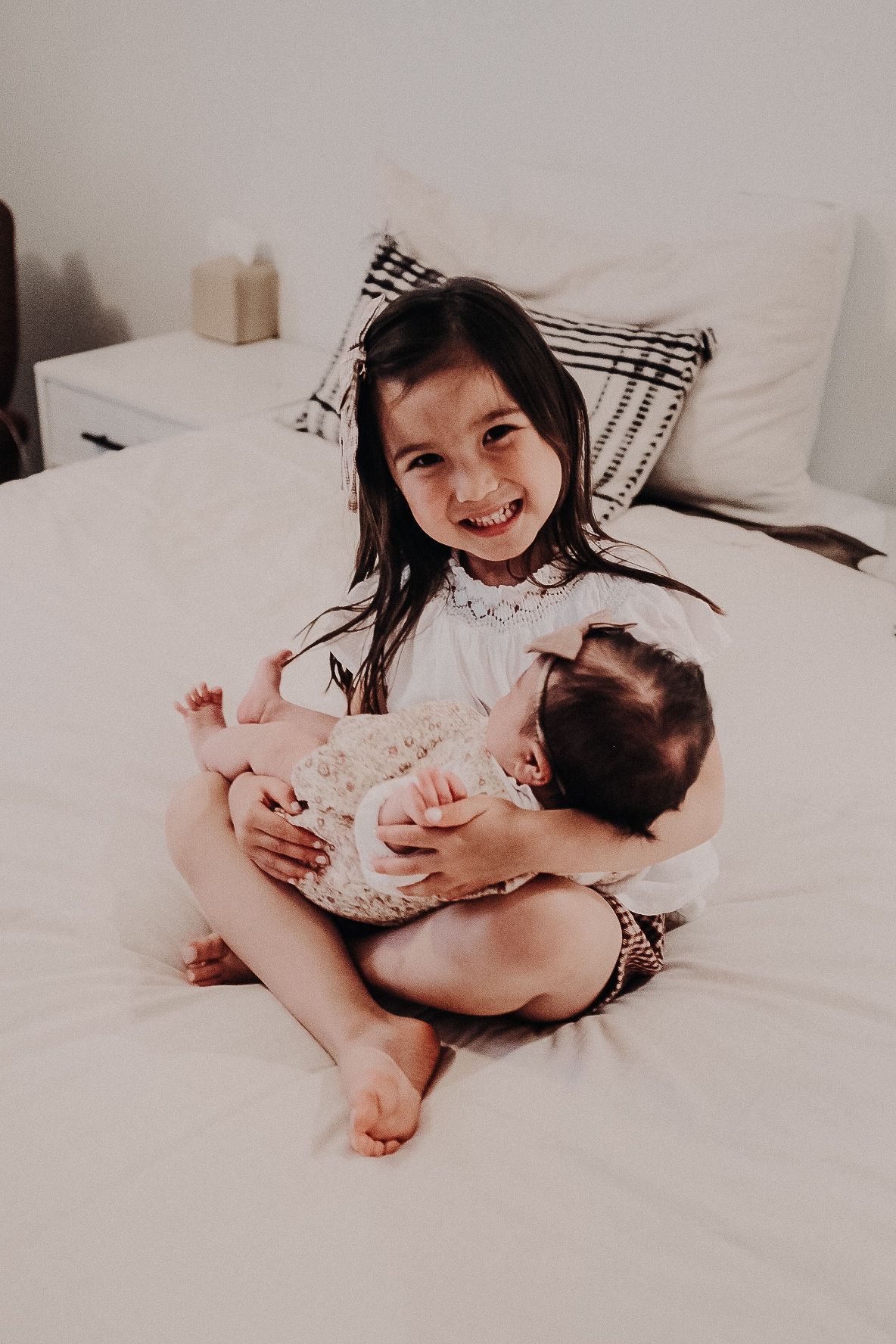 A tender moment on a white bed showing siblings sharing a sweet embrace.
