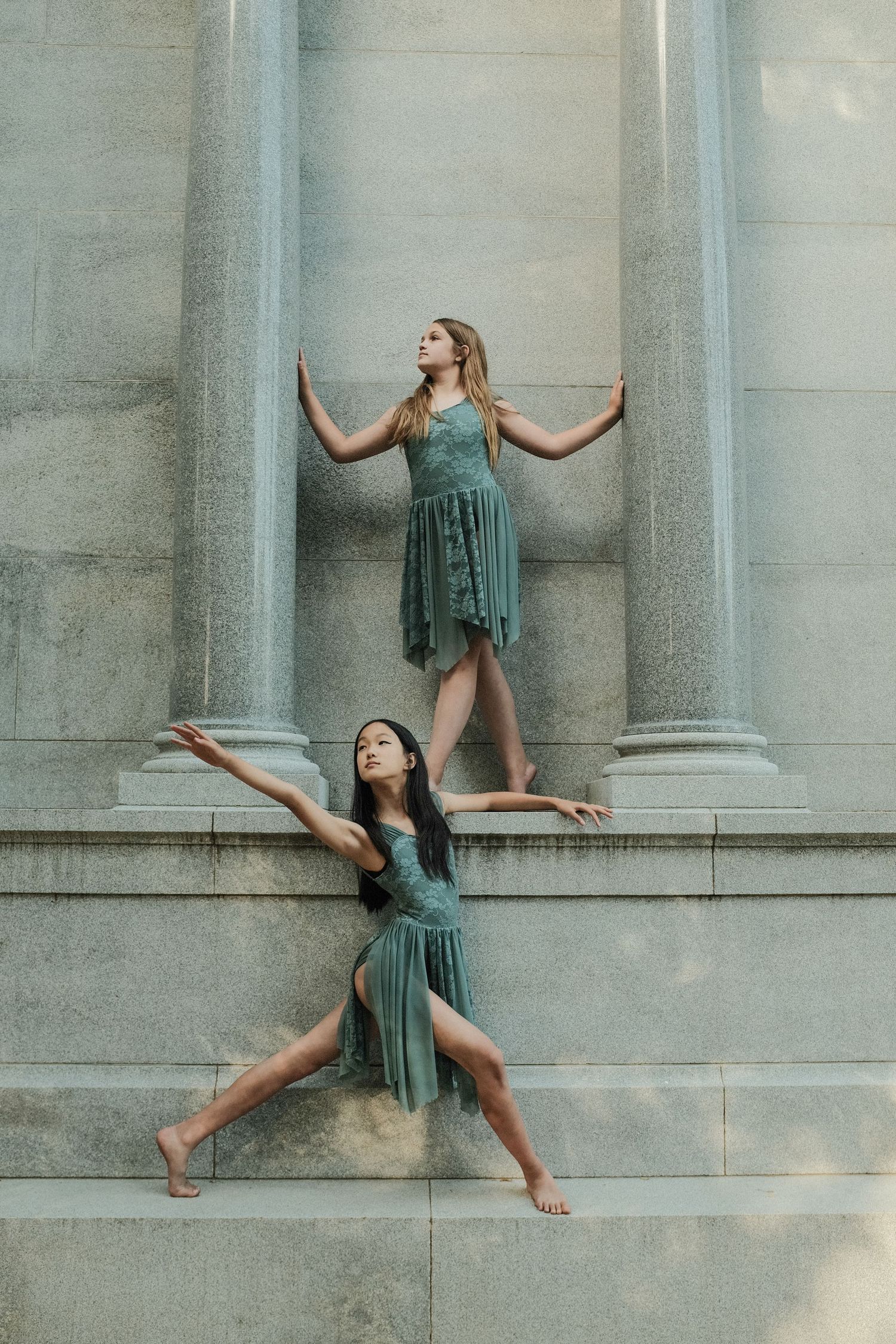 Dancers in matching teal dresses strike dramatic poses against a stone building with columns.