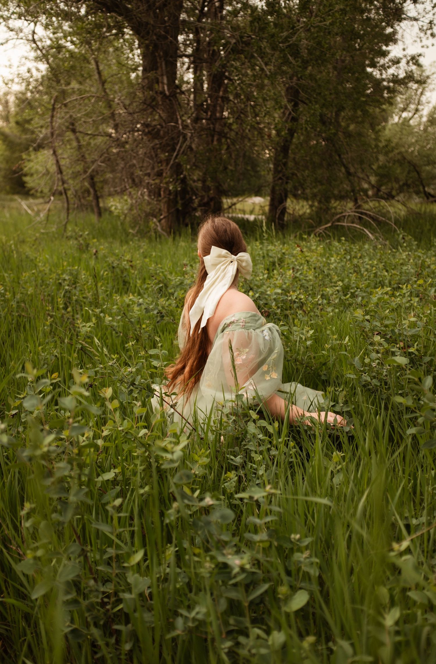 A dreamy portrait of someone in a vintage dress sitting among wildflowers in a meadow at sunset.