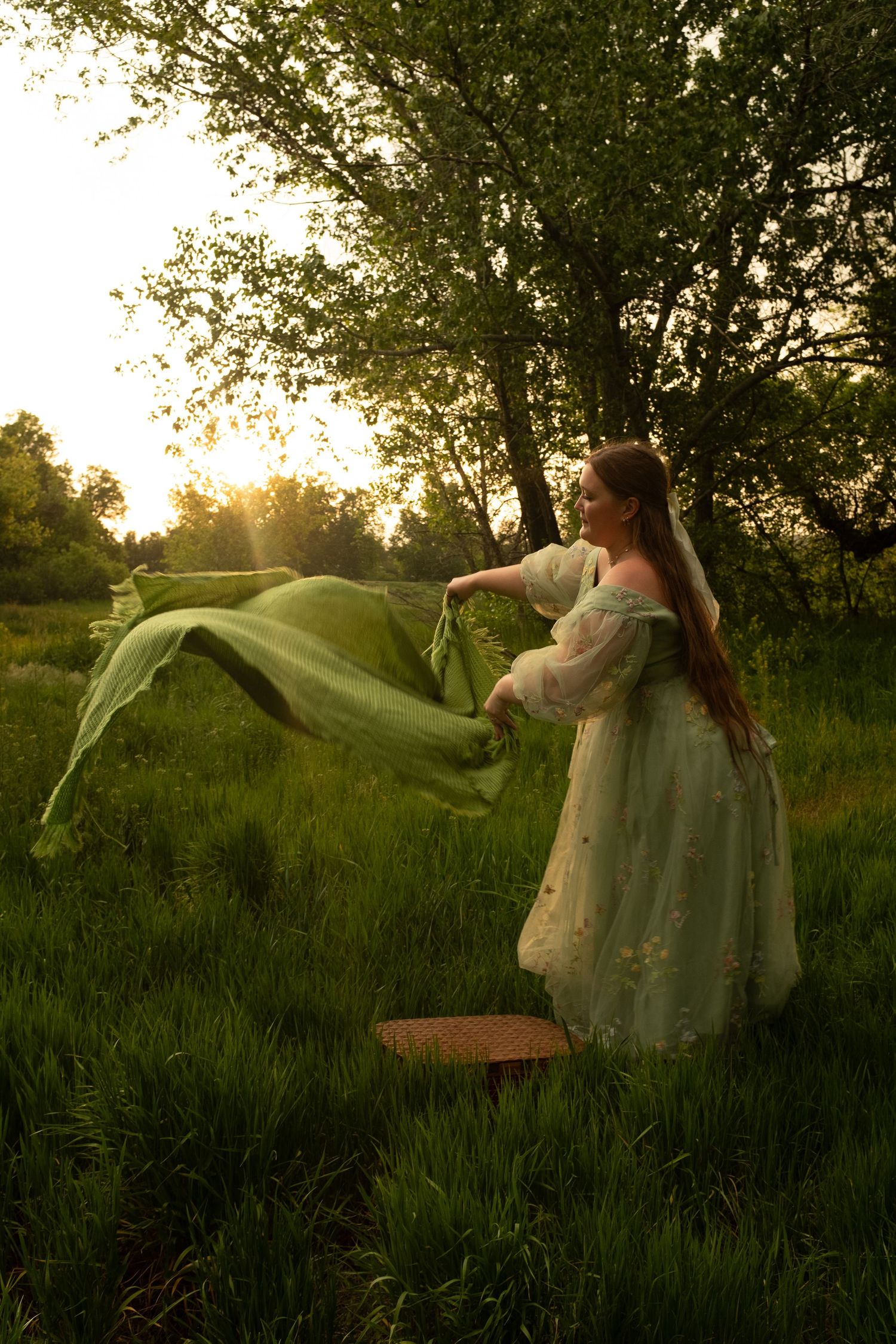 Person in flowing dress twirling fabric dramatically in a sunlit meadow at dusk.