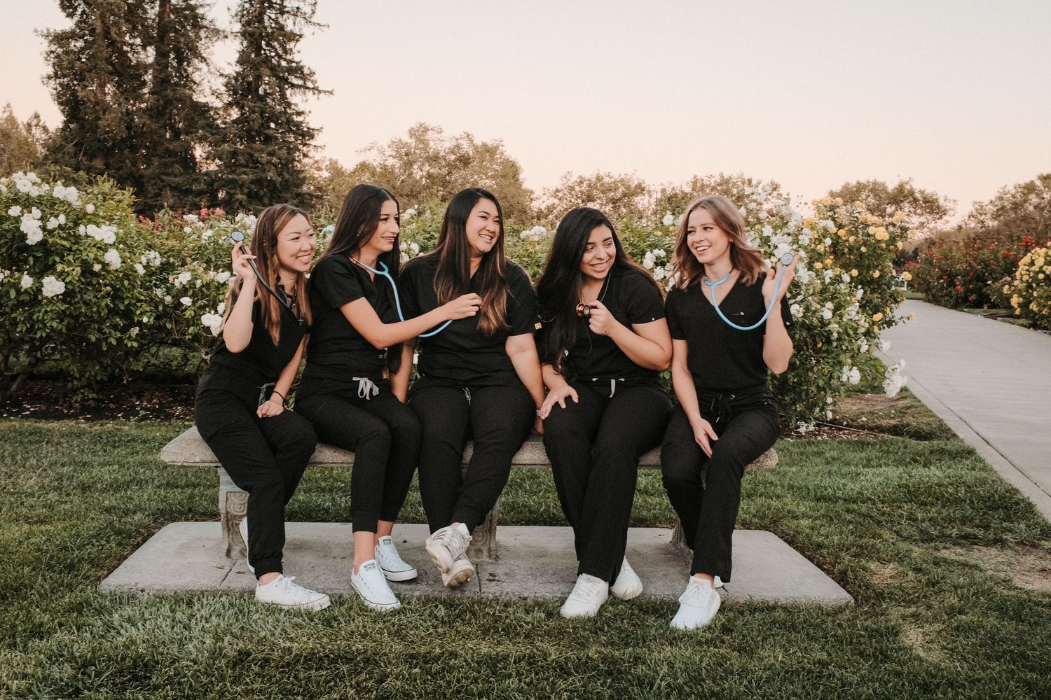 Group of graduates in black outfits sitting together outdoors during sunset.