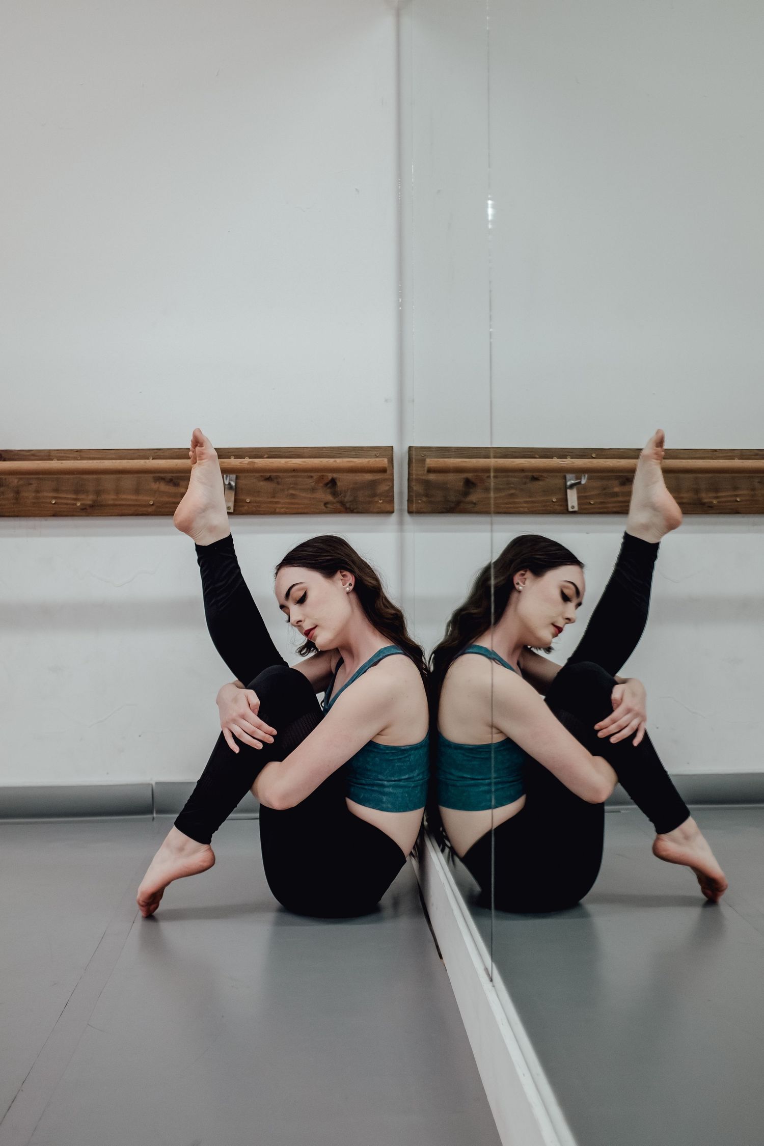 Dancer in black athletic wear poses with reflection in studio mirror showing flexibility.