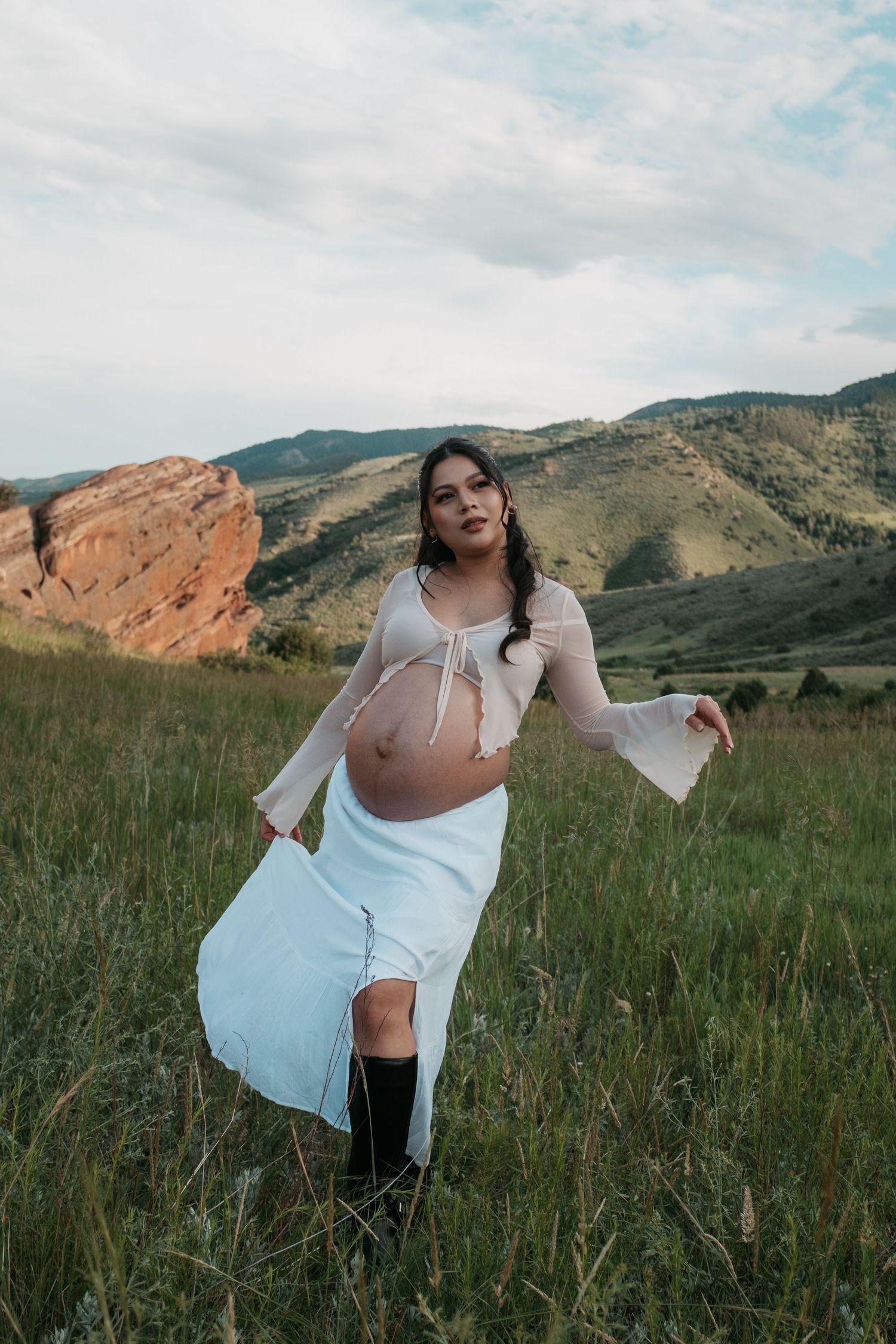 Dynamic maternity portrait with mountain landscape and flowing white dress.