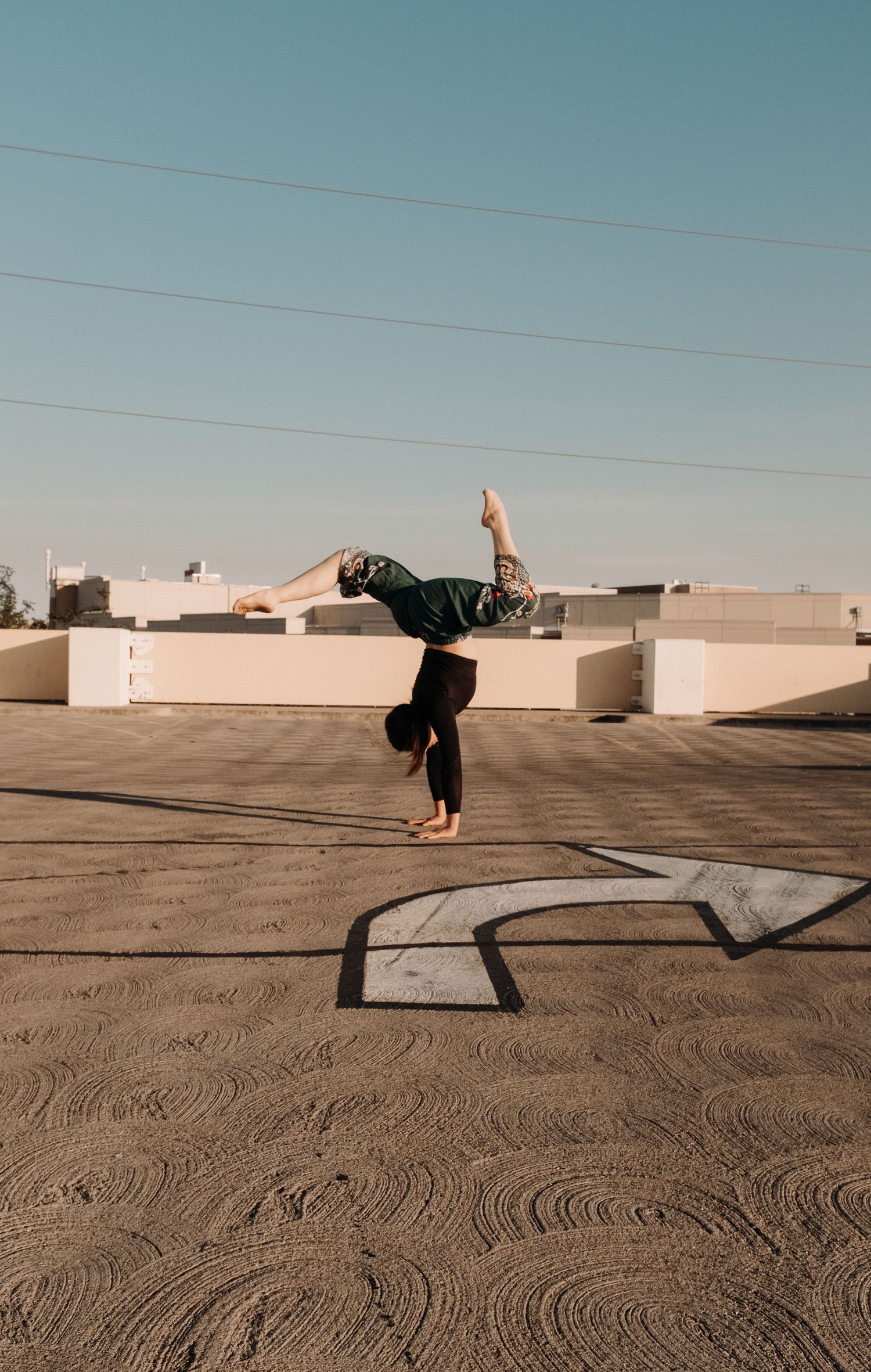 Dancer performs handstand on urban rooftop against blue sky with power lines.