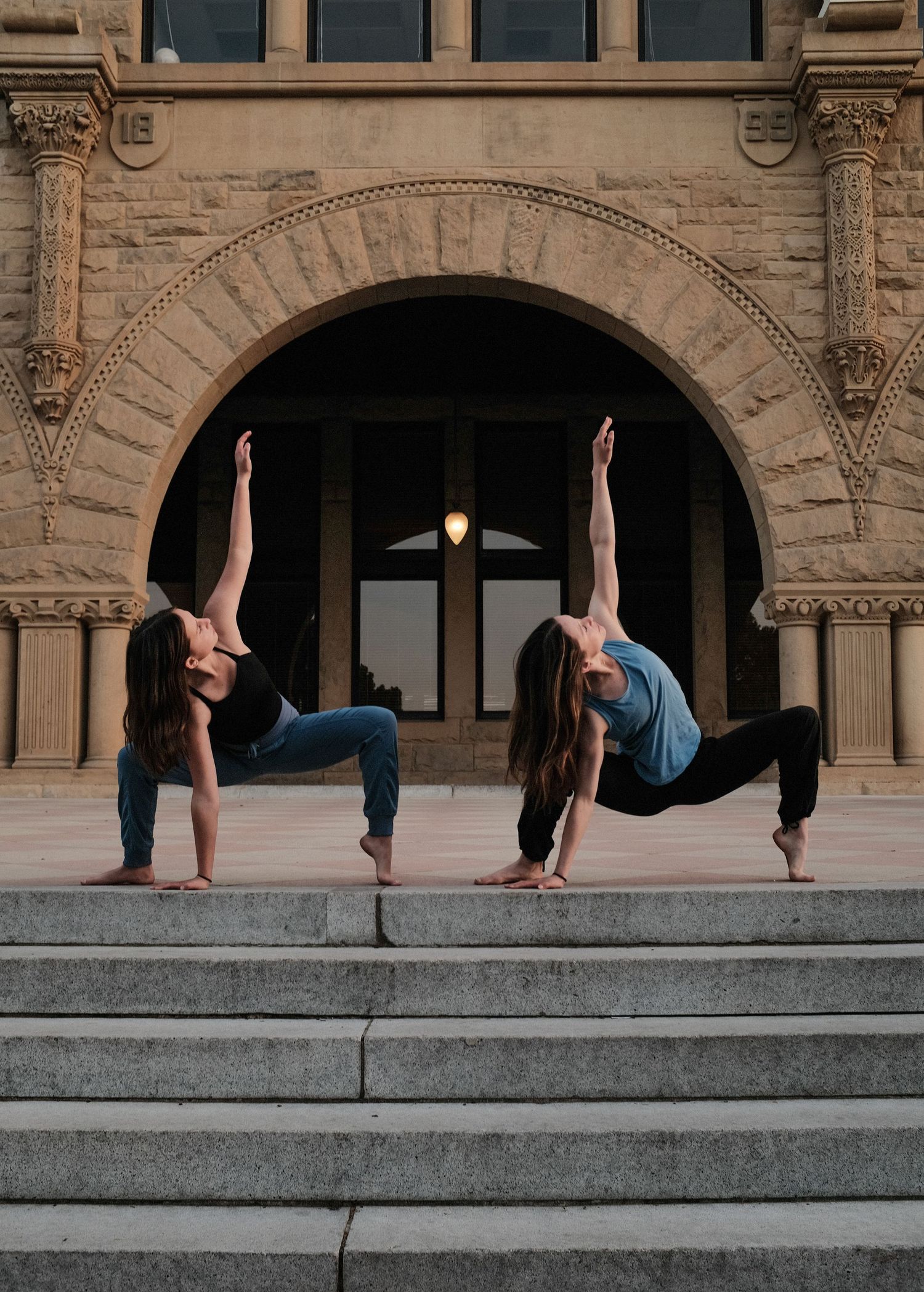 Two dancers perform synchronized poses on stone steps of a historical building.