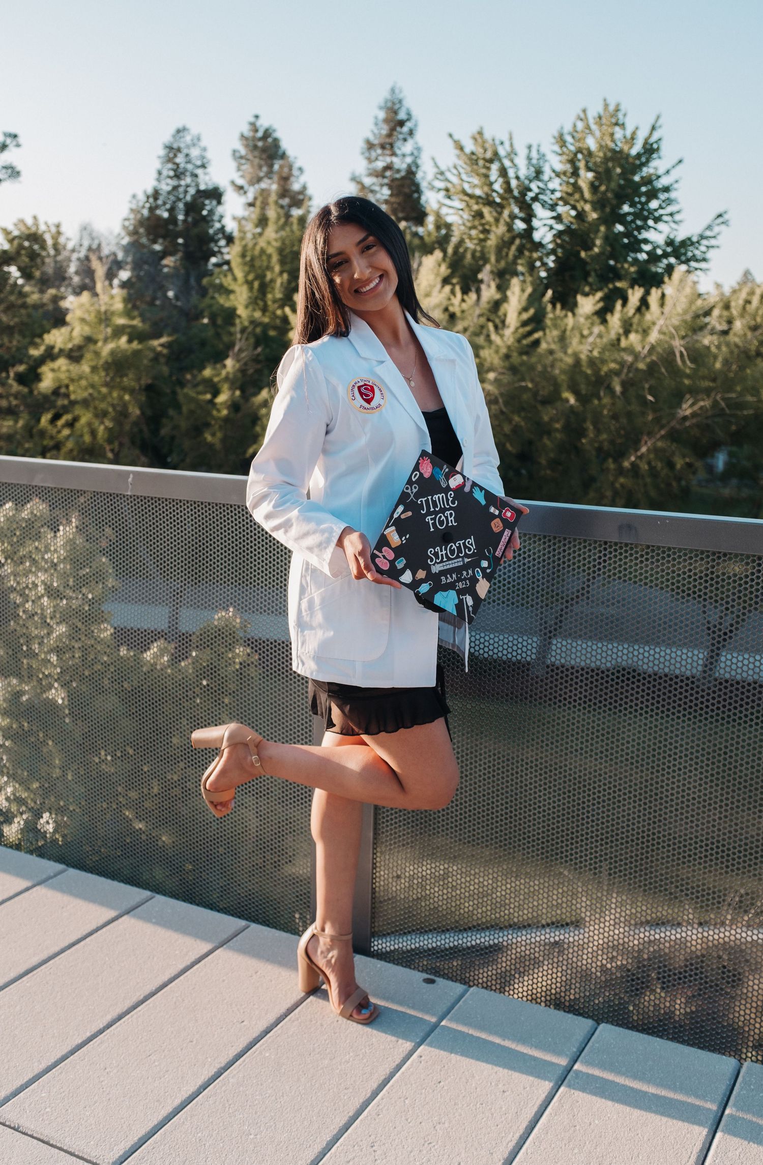 Graduate in white coat striking playful pose on outdoor deck.