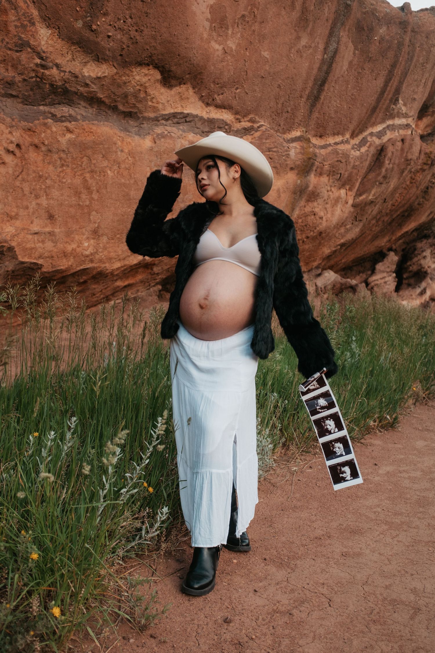 Pregnancy photoshoot featuring white dress and ultrasound photos against desert landscape.