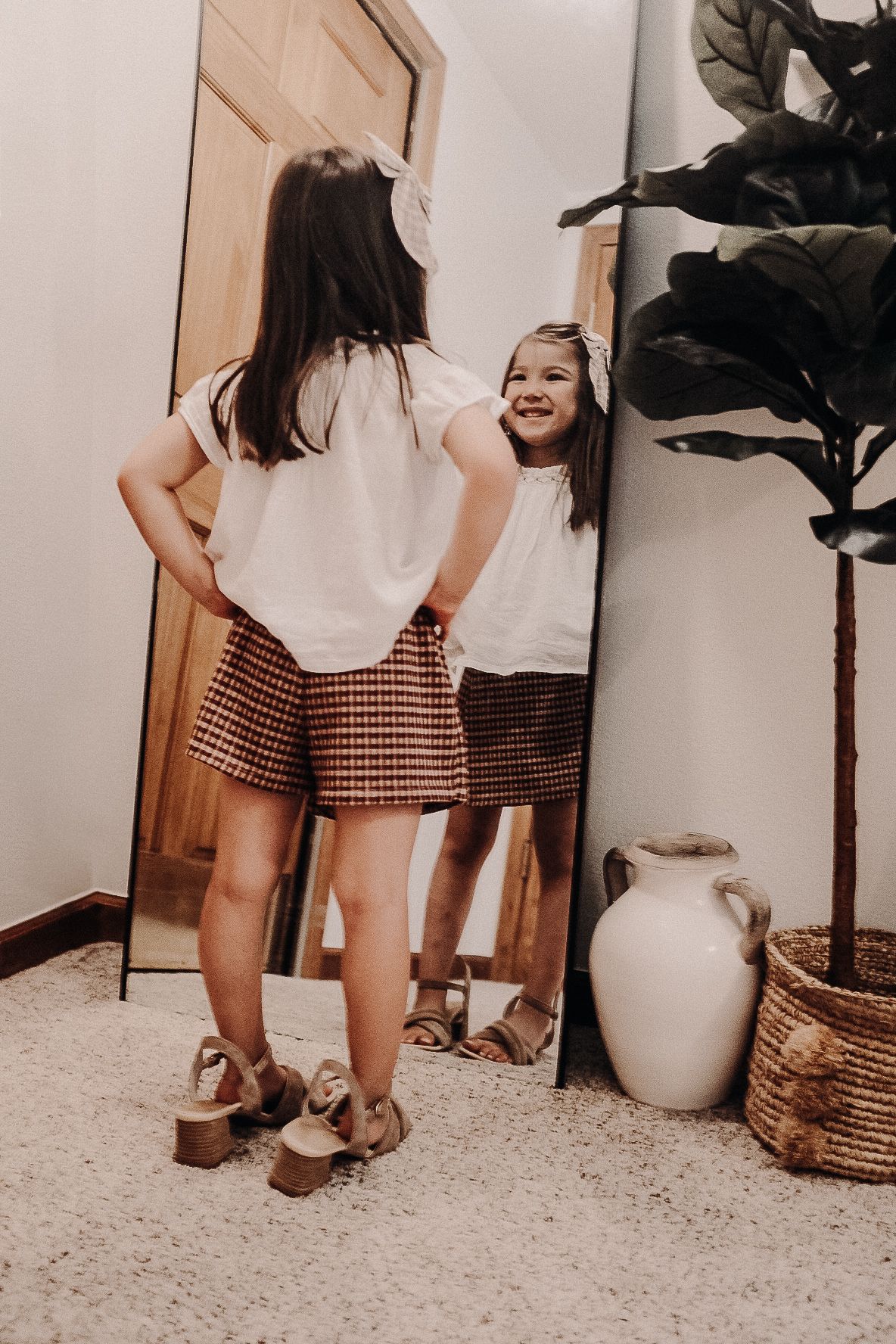 A reflection in a full-length mirror shows someone wearing a white top and checkered skirt.